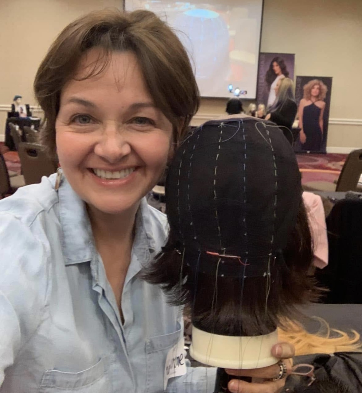 Woman smiling in a conference room with a mannequin head and a presentation screen in the background.