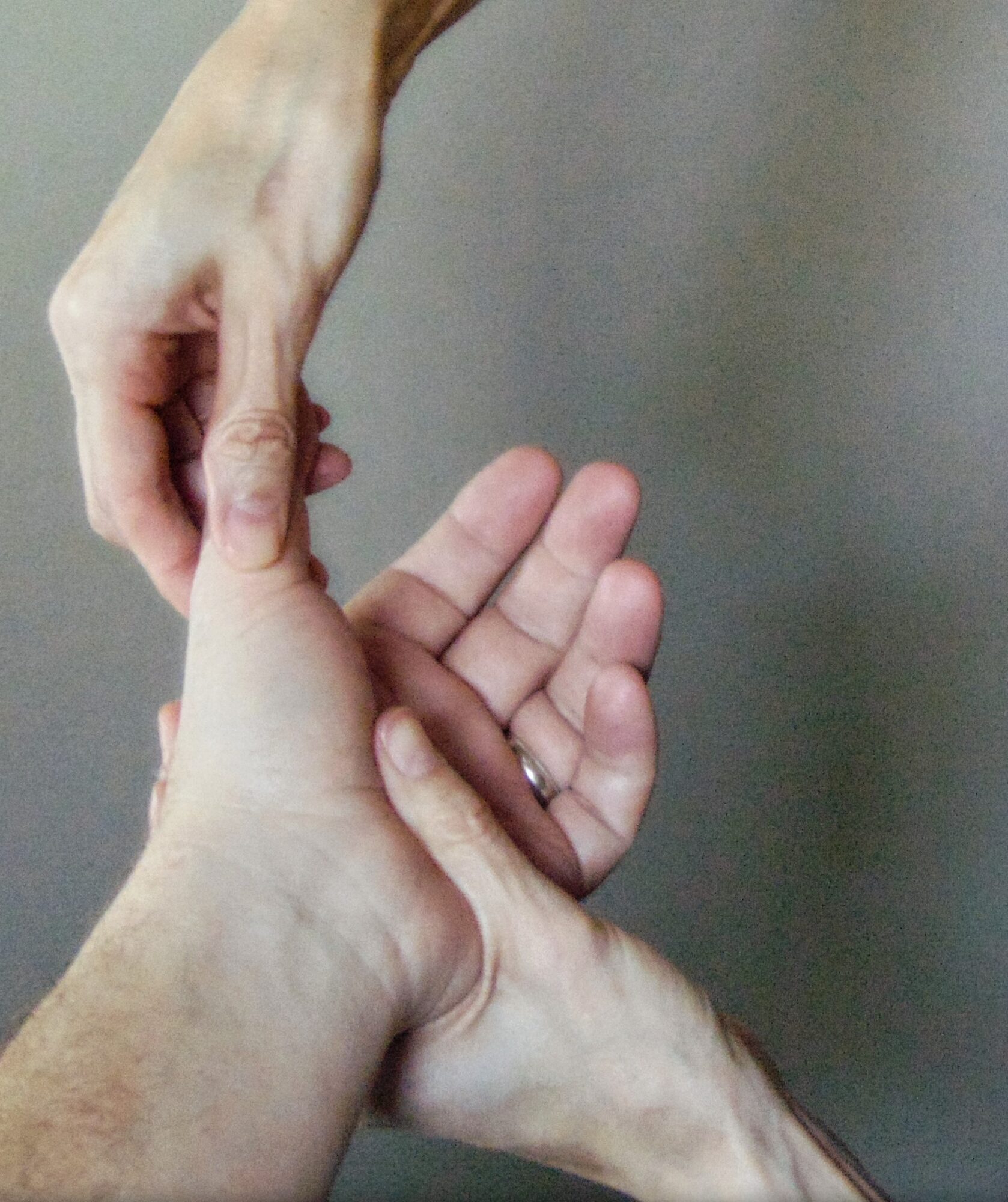 Two hands, one above the other, with fingers intertwined, against a plain background.