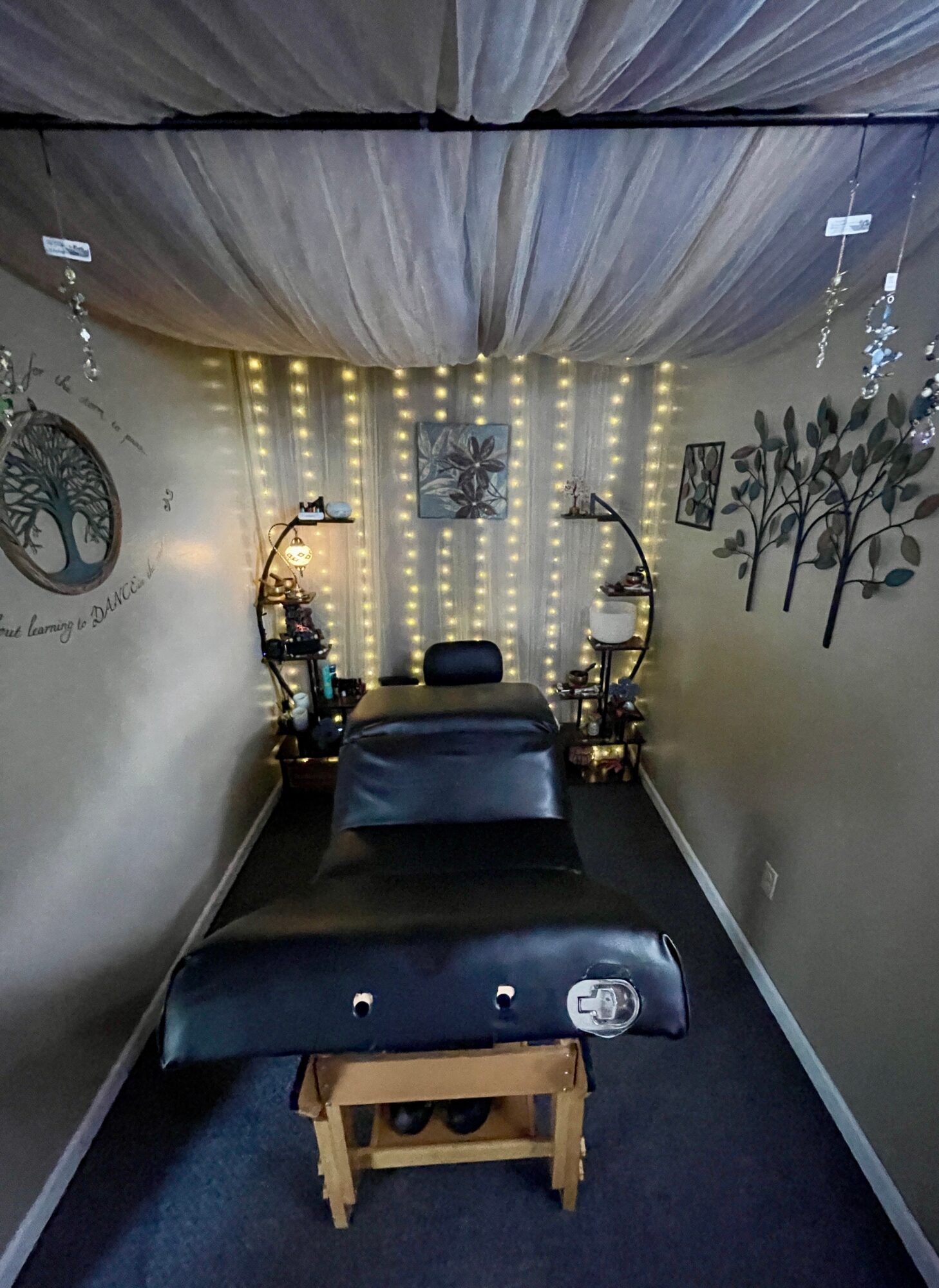 Massage table in a room with decorative wall art, string lights, and a ceiling with fabric draping.