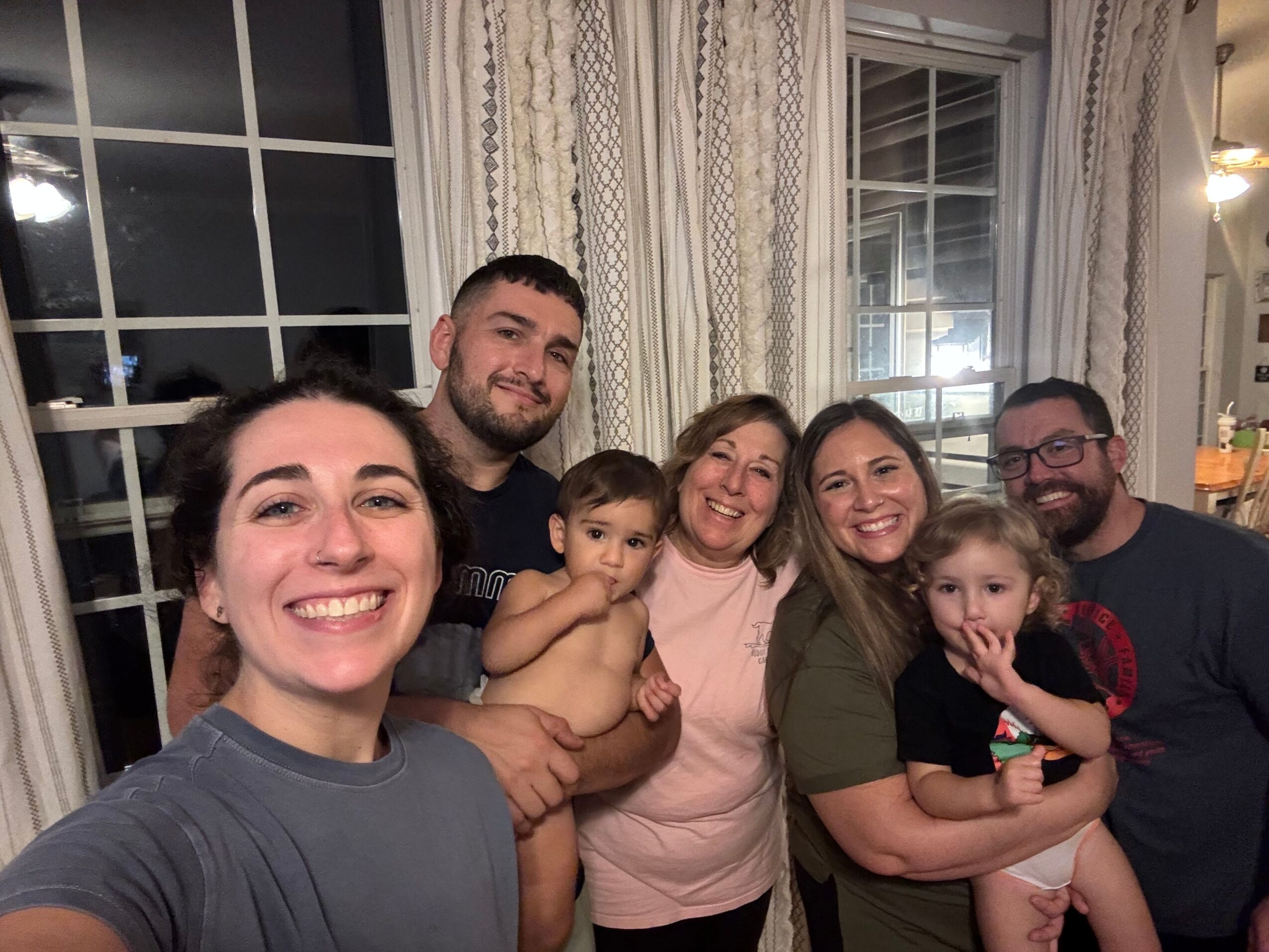 Group of six people smiling and posing indoors near a window, with some making peace signs.