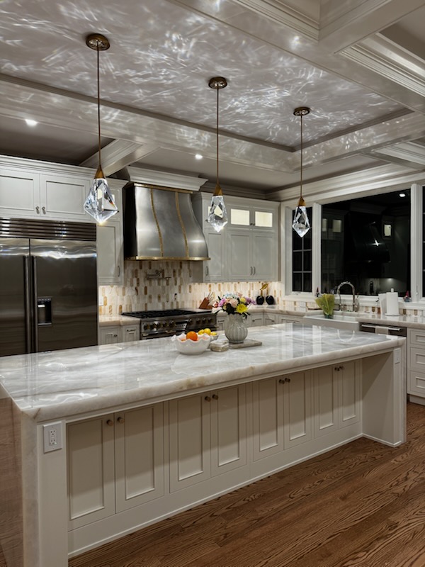 Modern kitchen with white island, pendant lights, stainless steel appliances, and a marble countertop.