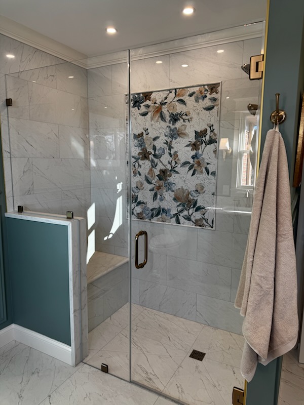 Glass shower enclosure with floral curtain, marble walls, and a towel hanging on a hook, in a bathroom.
