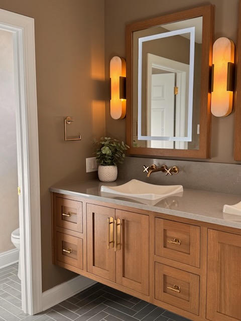Bathroom vanity with wooden cabinet, white sink, mirror, and wall-mounted lights, beige wall, and tiled floor.
