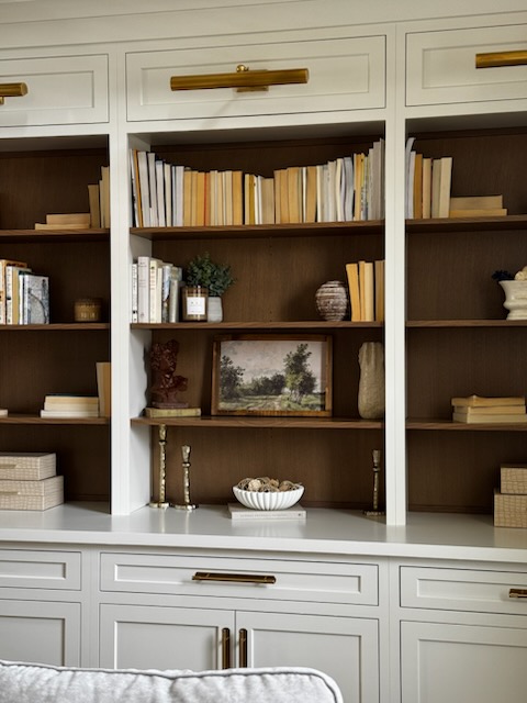 White bookshelf with books, decorative items, and a landscape painting, with drawers below and gold handles.