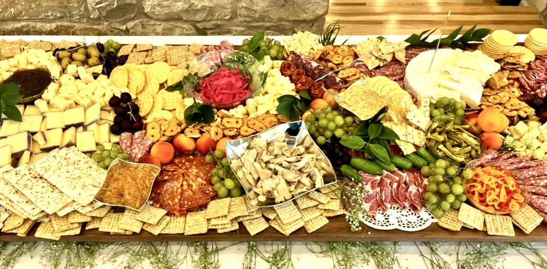 Assorted cheeses, fruits, crackers, and nuts arranged on a platter with flowers and greenery.