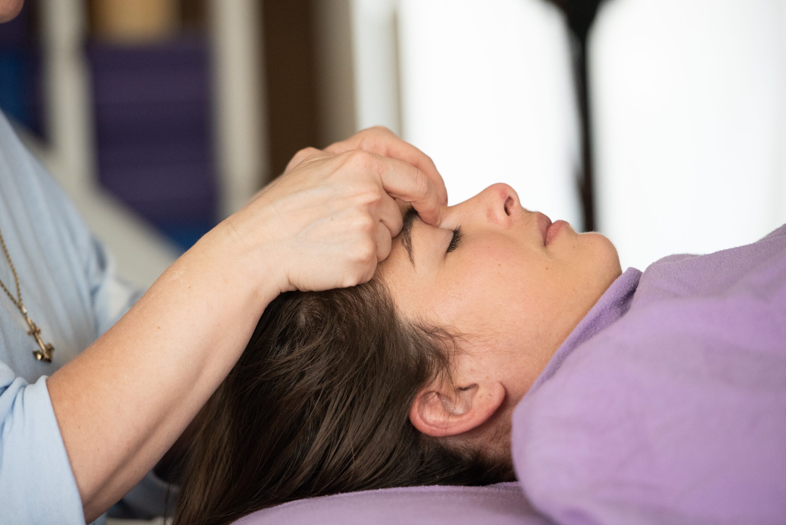Person lying down with eyes closed, receiving a forehead massage or treatment from another person.