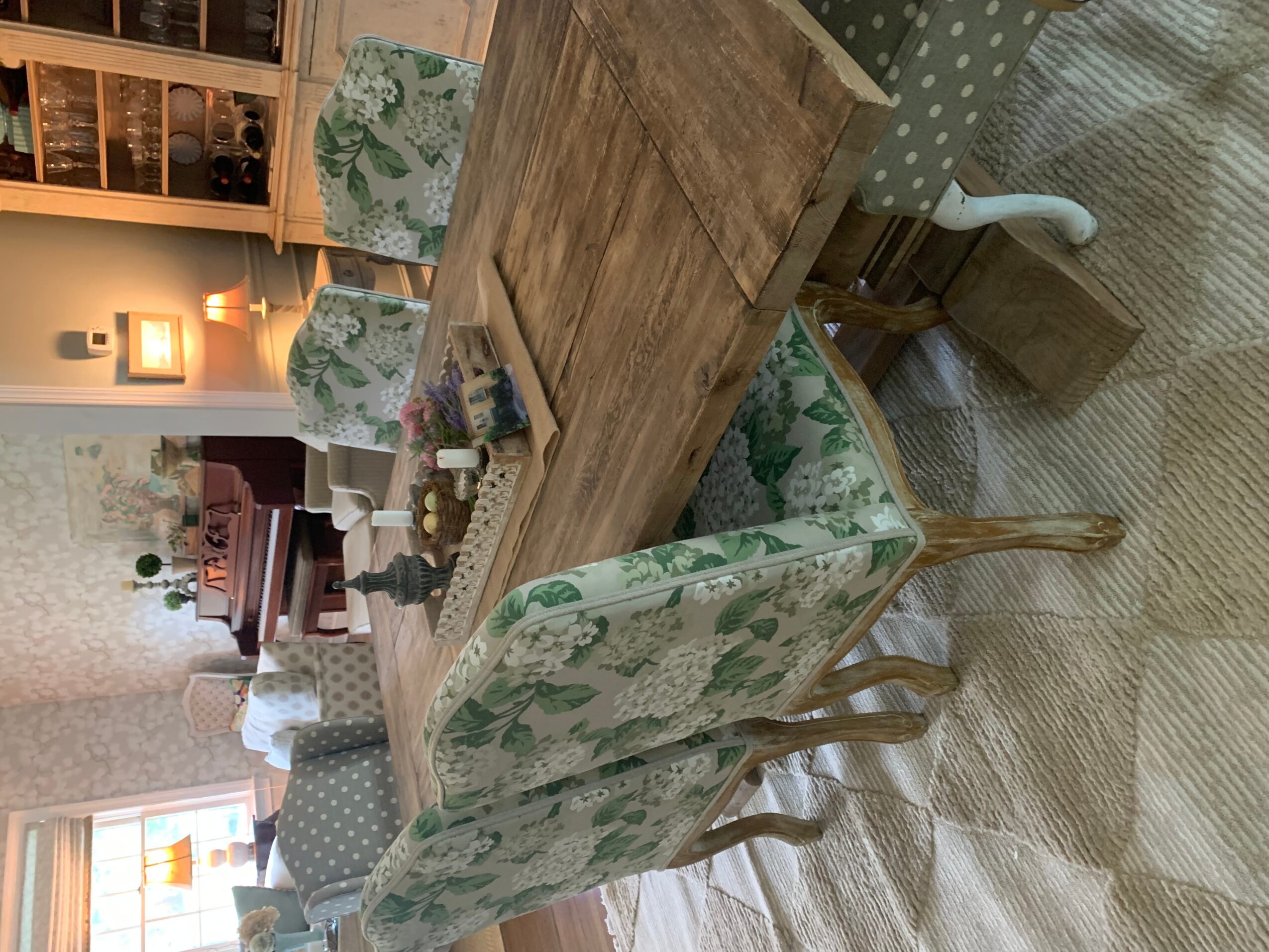 Dining room with wooden table, floral upholstered chairs, and a sideboard with decorative items, illuminated by warm lighting.