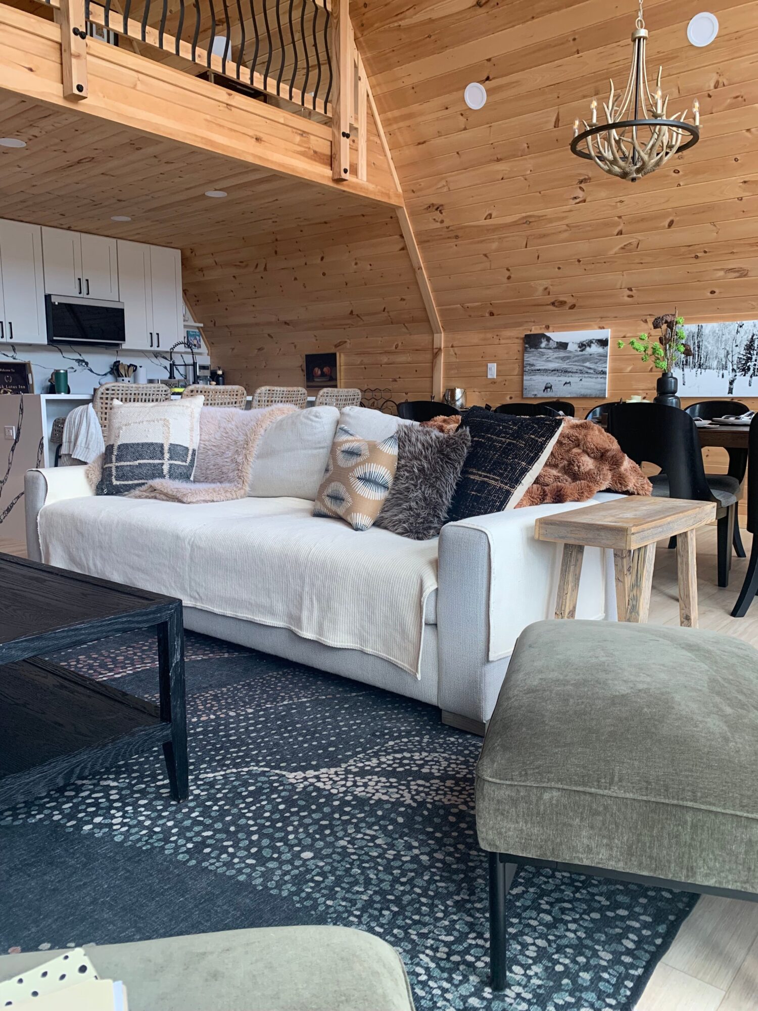Living room with wooden ceiling, sofa with cushions, coffee table, and a patterned rug.
