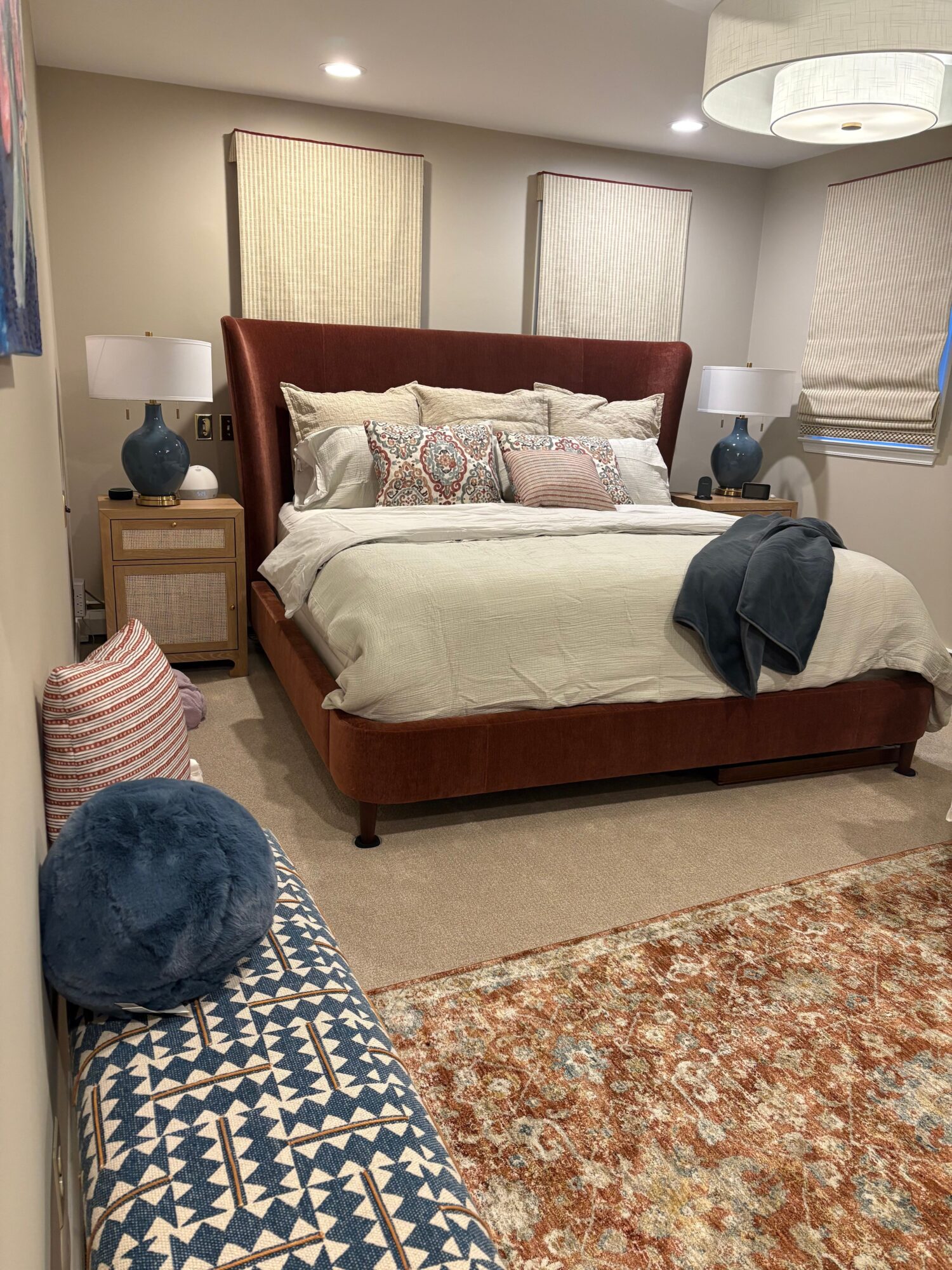 Bedroom with bed, pillows, nightstand, and a person leaning over the bed, viewed from the foot of the bed.