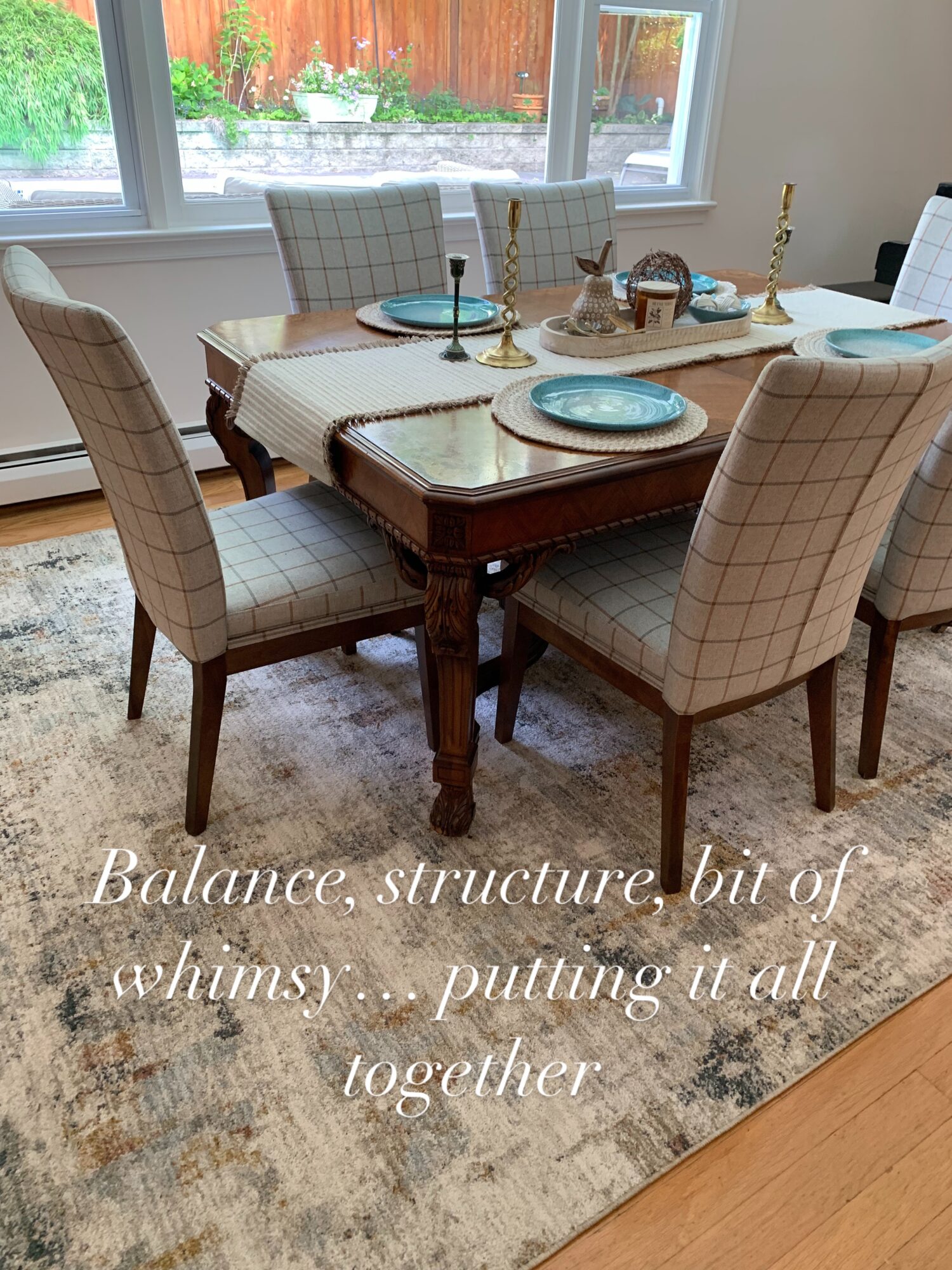 Dining table with six upholstered chairs, set with plates, glasses, and a centerpiece, near a window with a view outside.