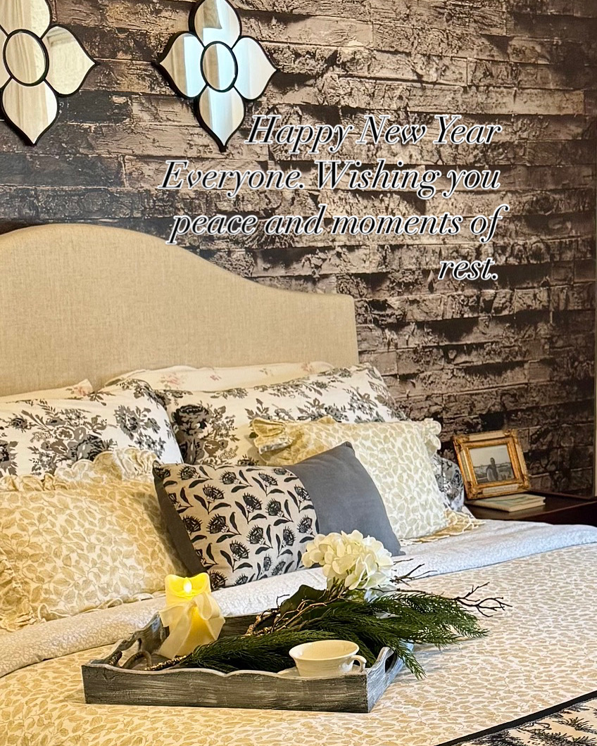 Decorated bedroom with a bed, pillows, flowers, and a tray, against a brick wall with New Year message and ornaments.