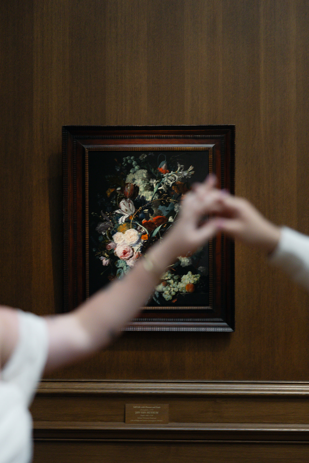 Two children reach towards a framed floral painting on a wooden wall, their hands blurred in motion.