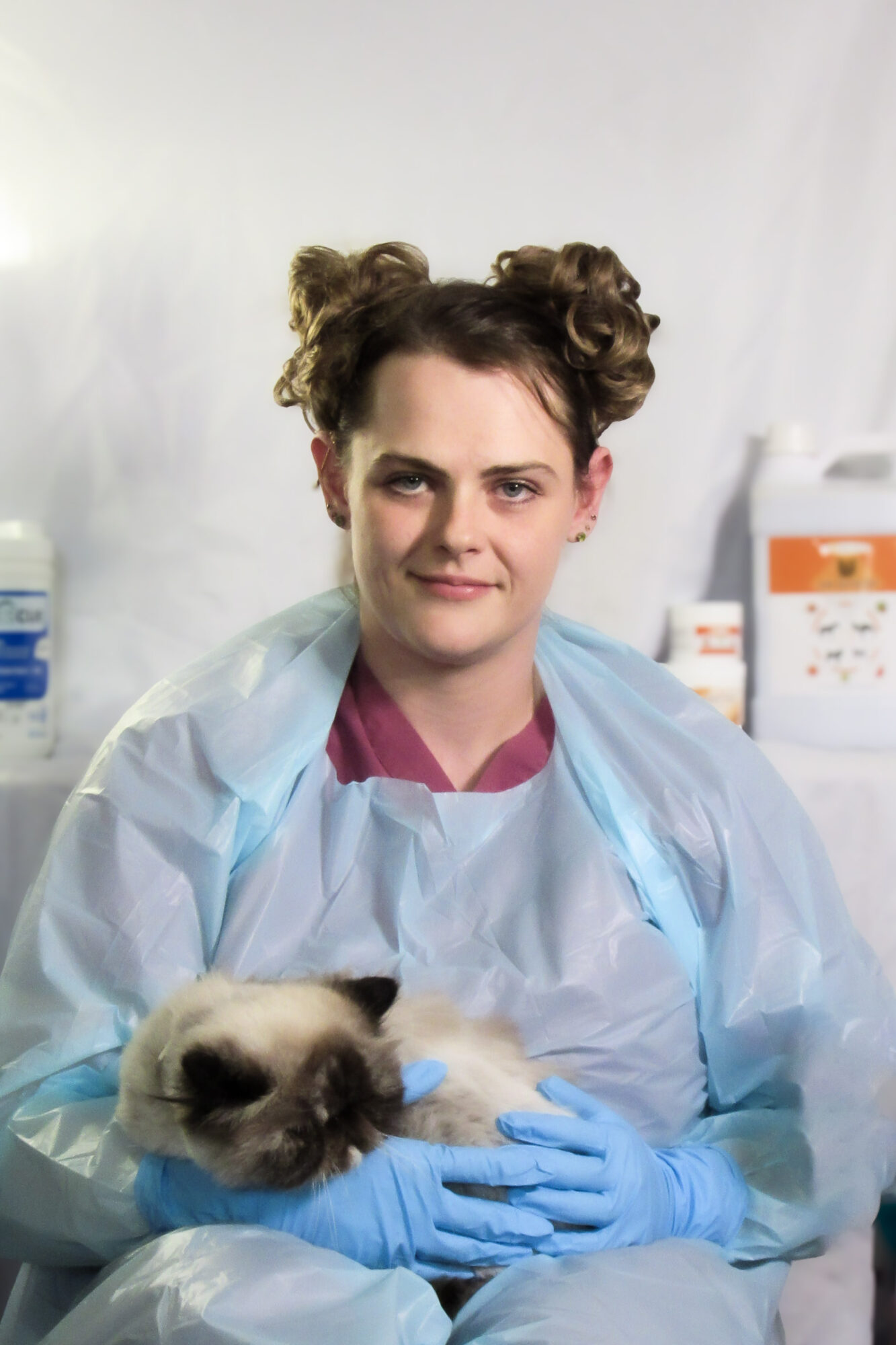 Young woman in medical attire holding a cat, with medical equipment in the background.
