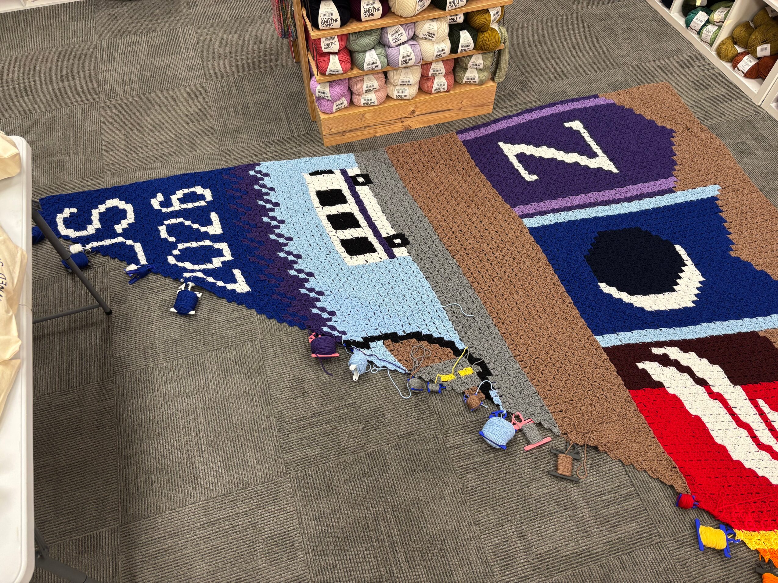 Partially completed quilt with school-themed designs and colorful borders on a carpeted floor.
