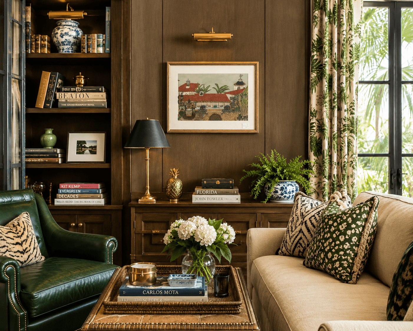Living room with bookshelf, framed artwork, green and beige sofas, and a coffee table with flowers.