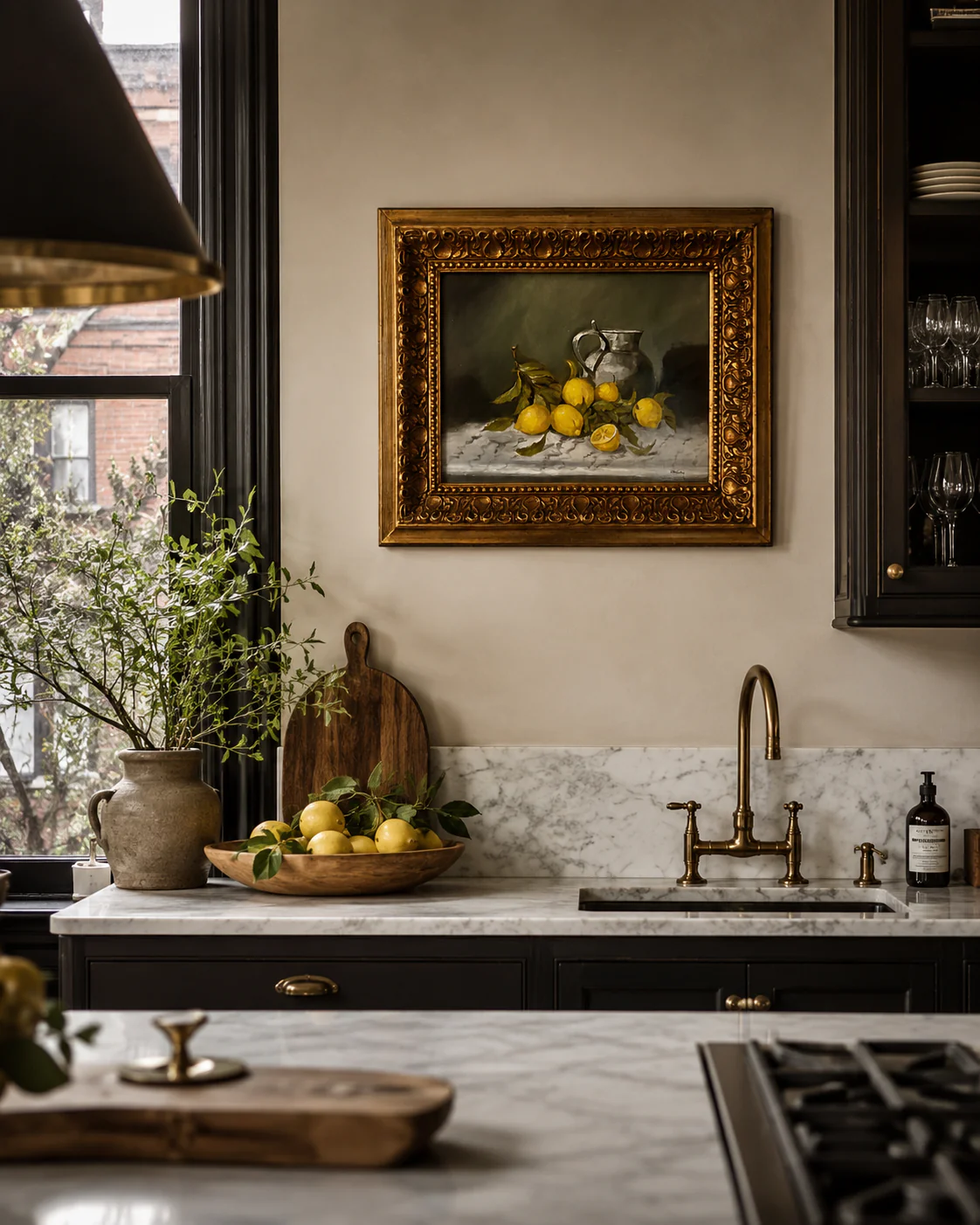 Kitchen with a framed still life painting of lemons, a marble countertop, a sink, and a window with natural light.