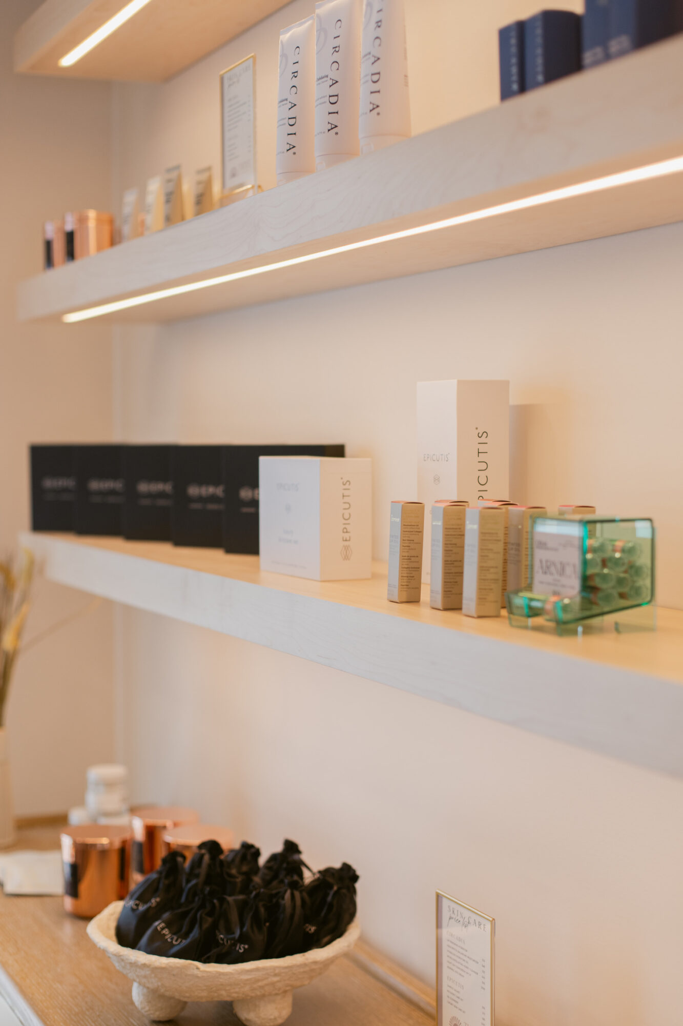 Two white shelves with various skincare and cosmetic products, some in boxes and bottles, against a light-colored wall.