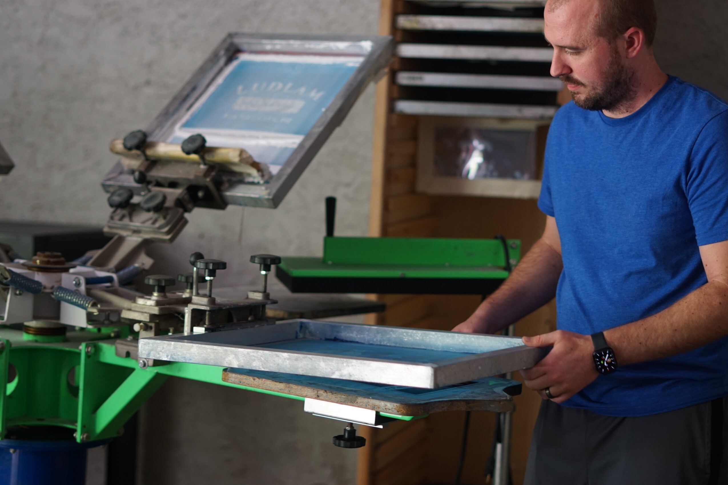 Man in blue shirt working with a large machine in a workshop setting.
