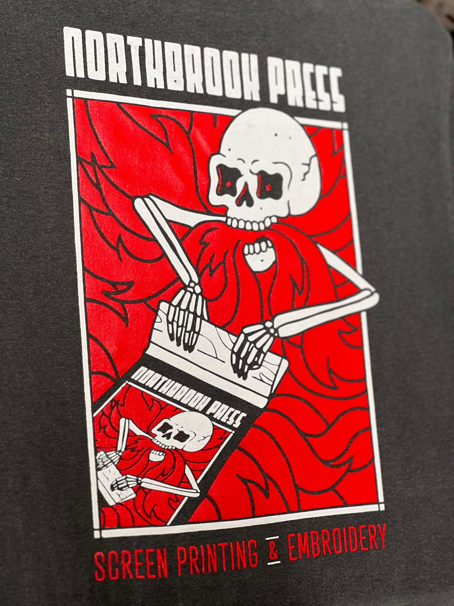 Skull with red cape and wings, playing keyboard, with text 'Northwood Press' and 'Screen Printing & Embroidery'.