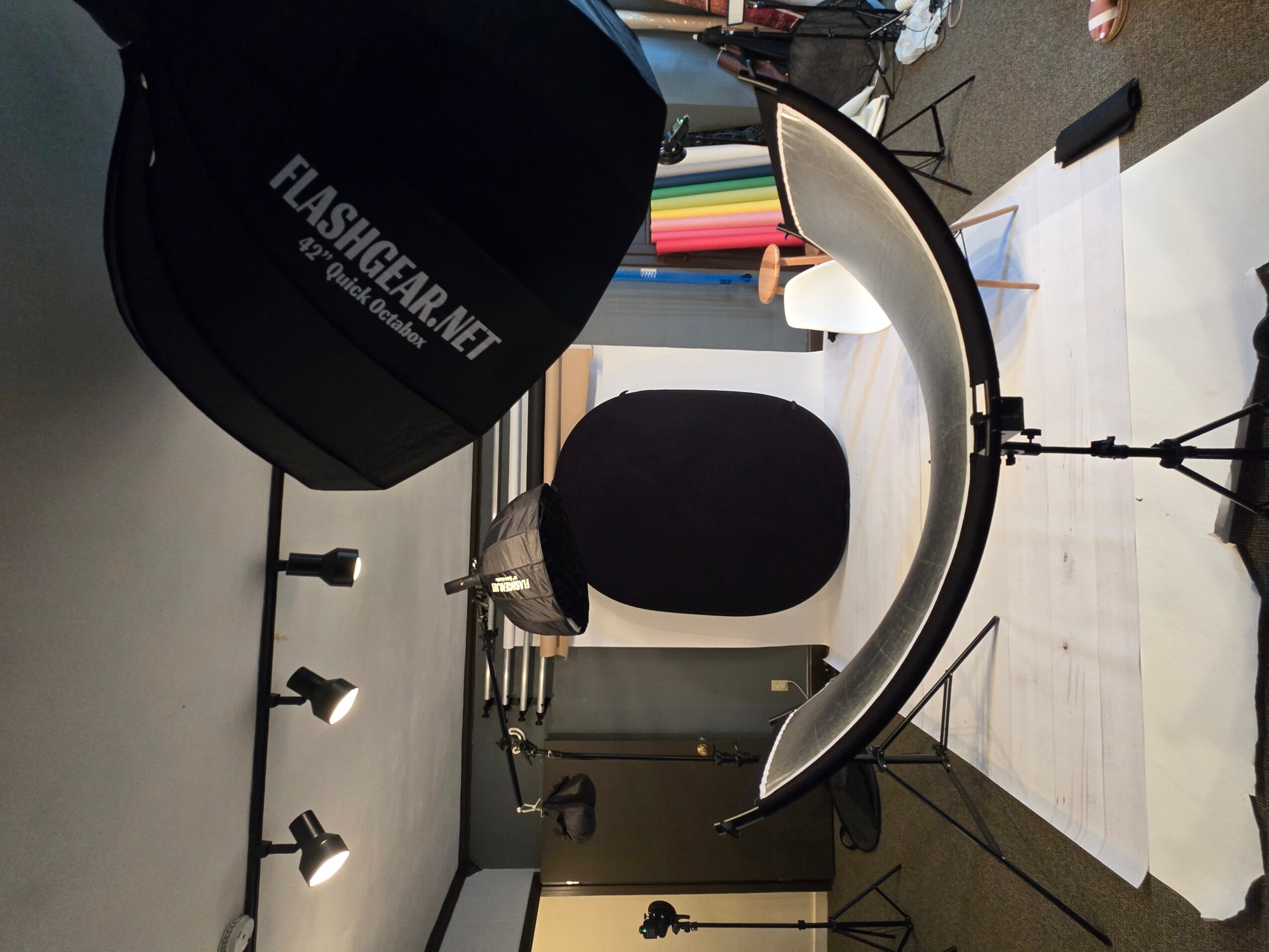 Desk with a black chair, a curved light, a camera bag, and various items on the surface.