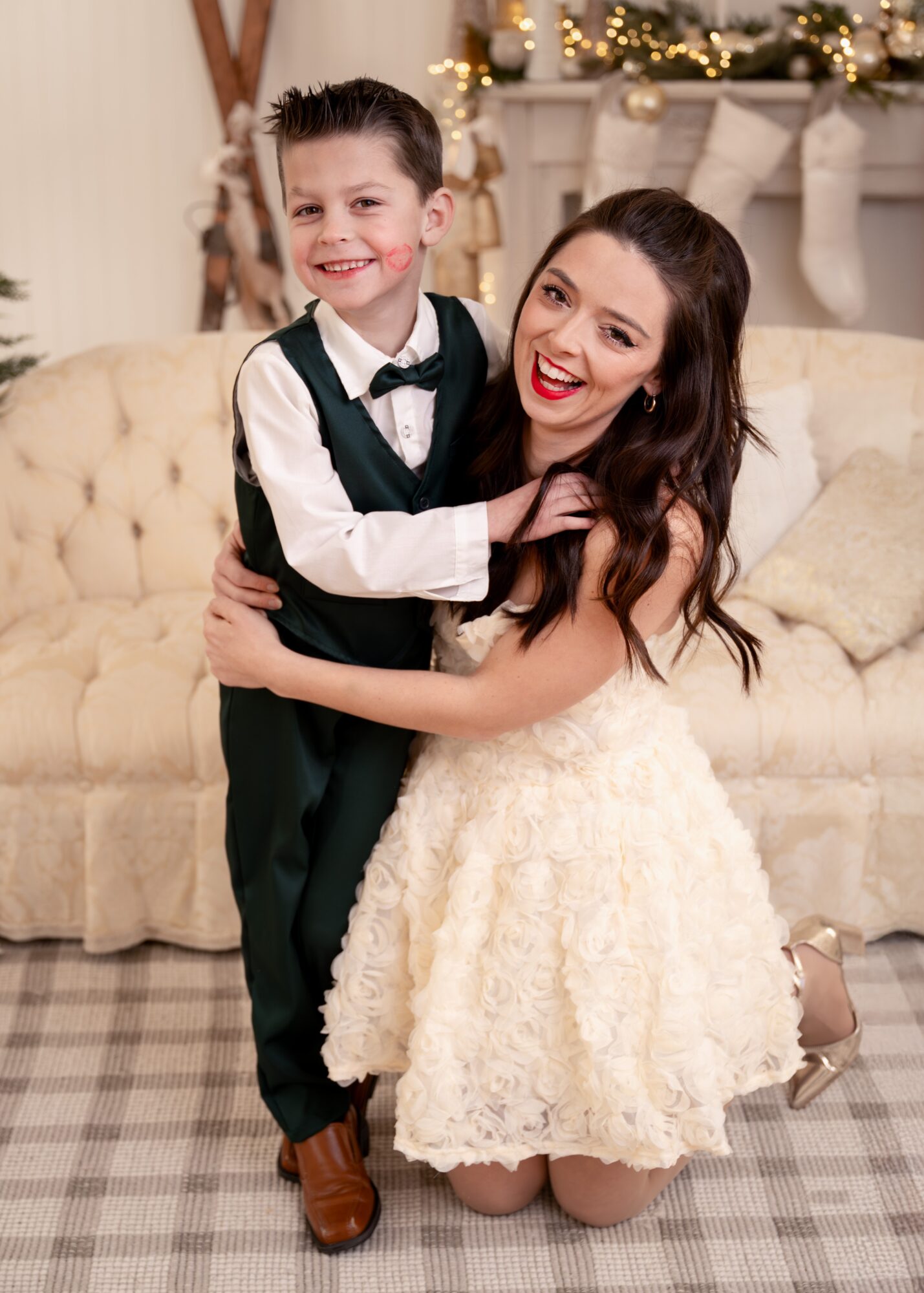 A woman and a young boy are smiling and hugging on a sofa in a festive room with stockings and decorations.