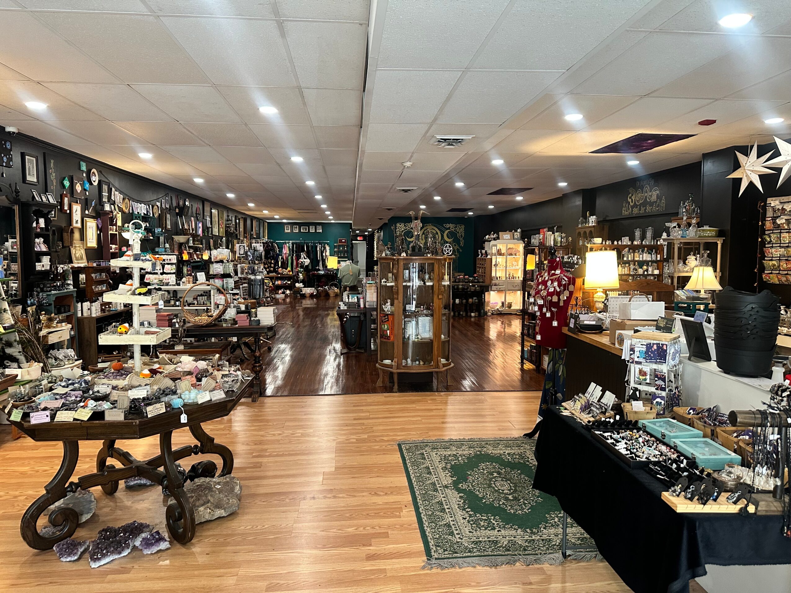 Interior of a store with shelves, display tables, and a patterned rug, filled with various items for sale.