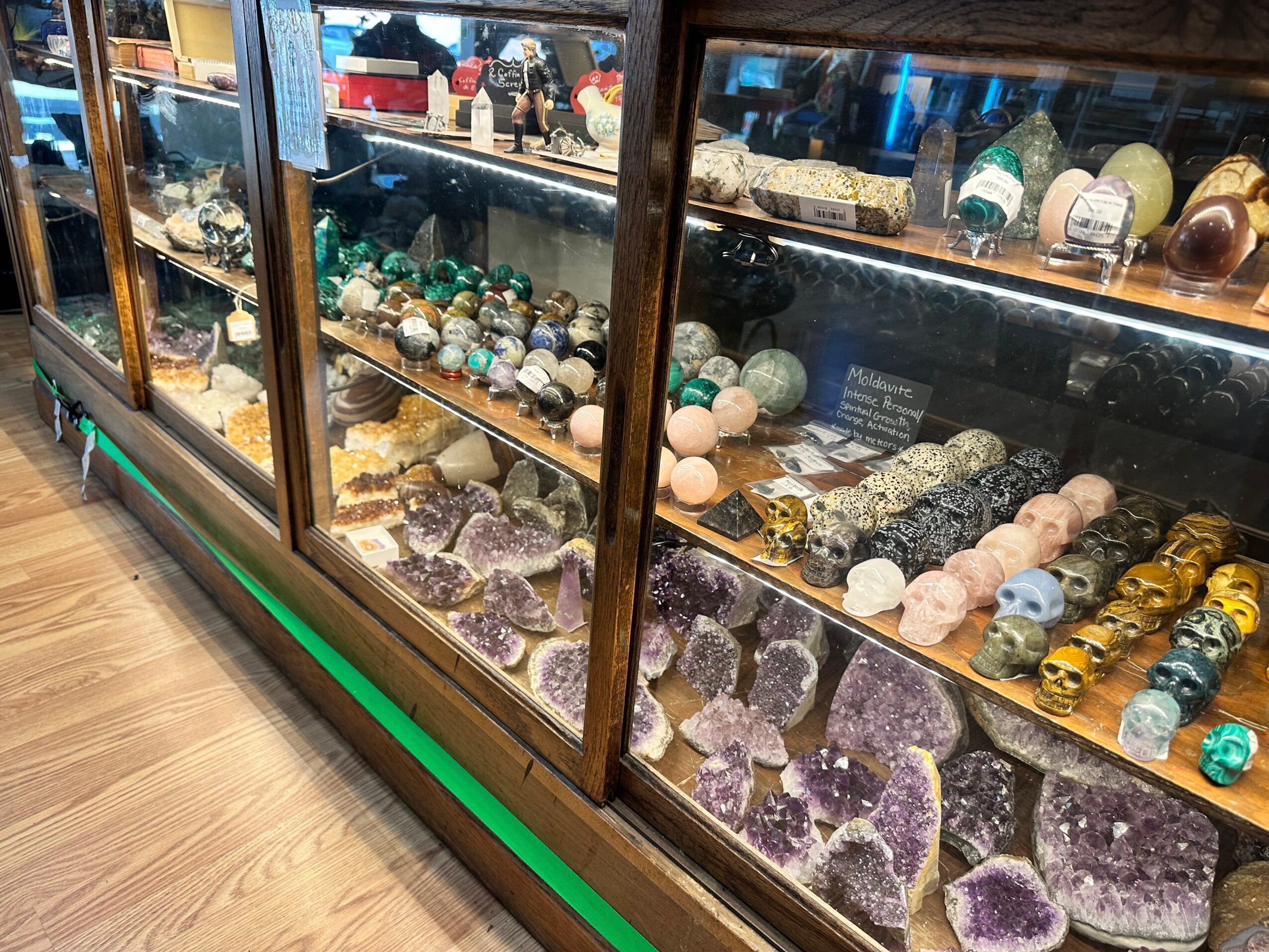 Display case with various mineral and crystal specimens, including amethyst, quartz, and other colorful stones, on glass shelves.