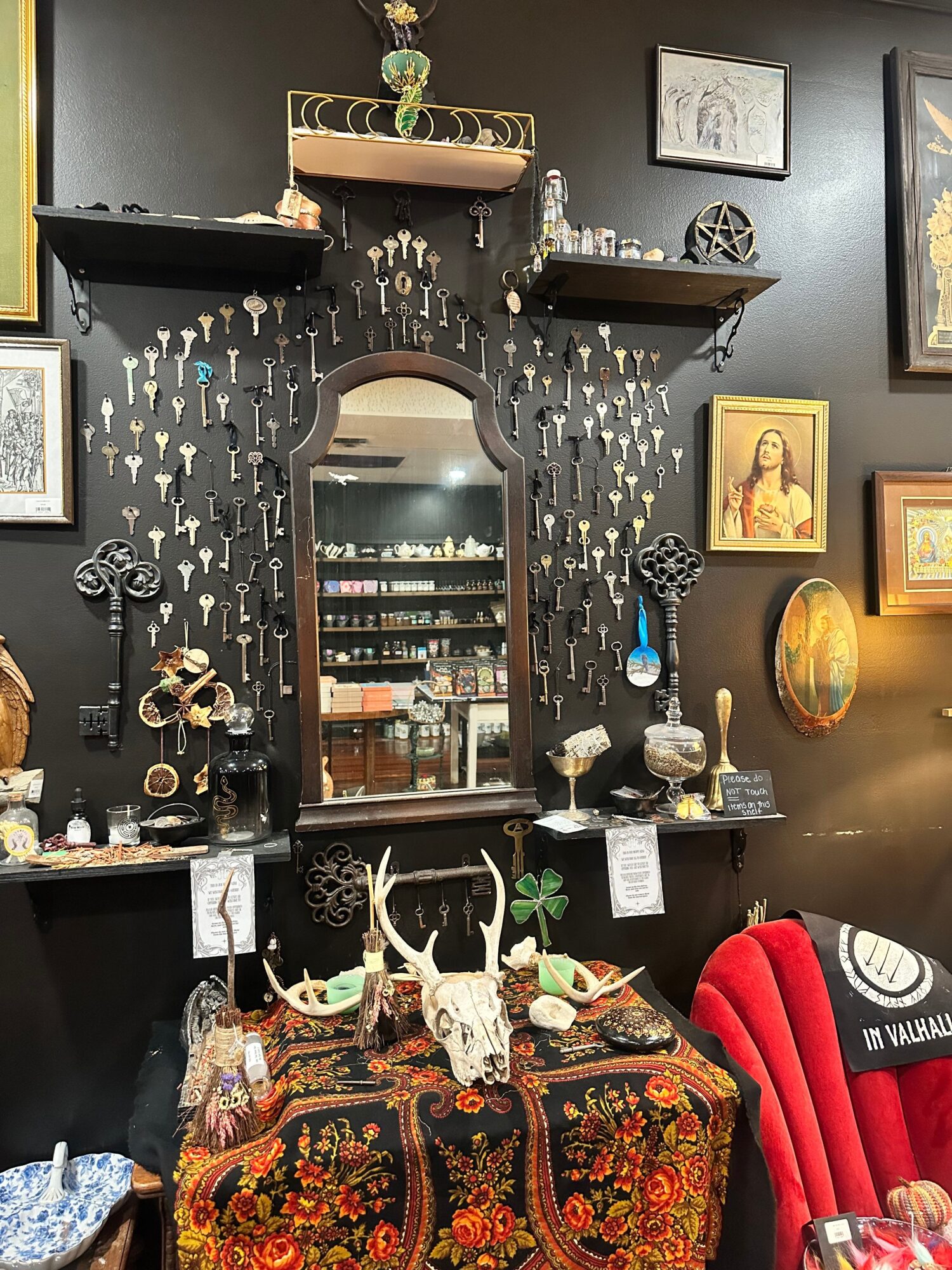 Decorative display with a mirror, framed pictures, and various objects on a black wall, including a red chair and patterned fabric.