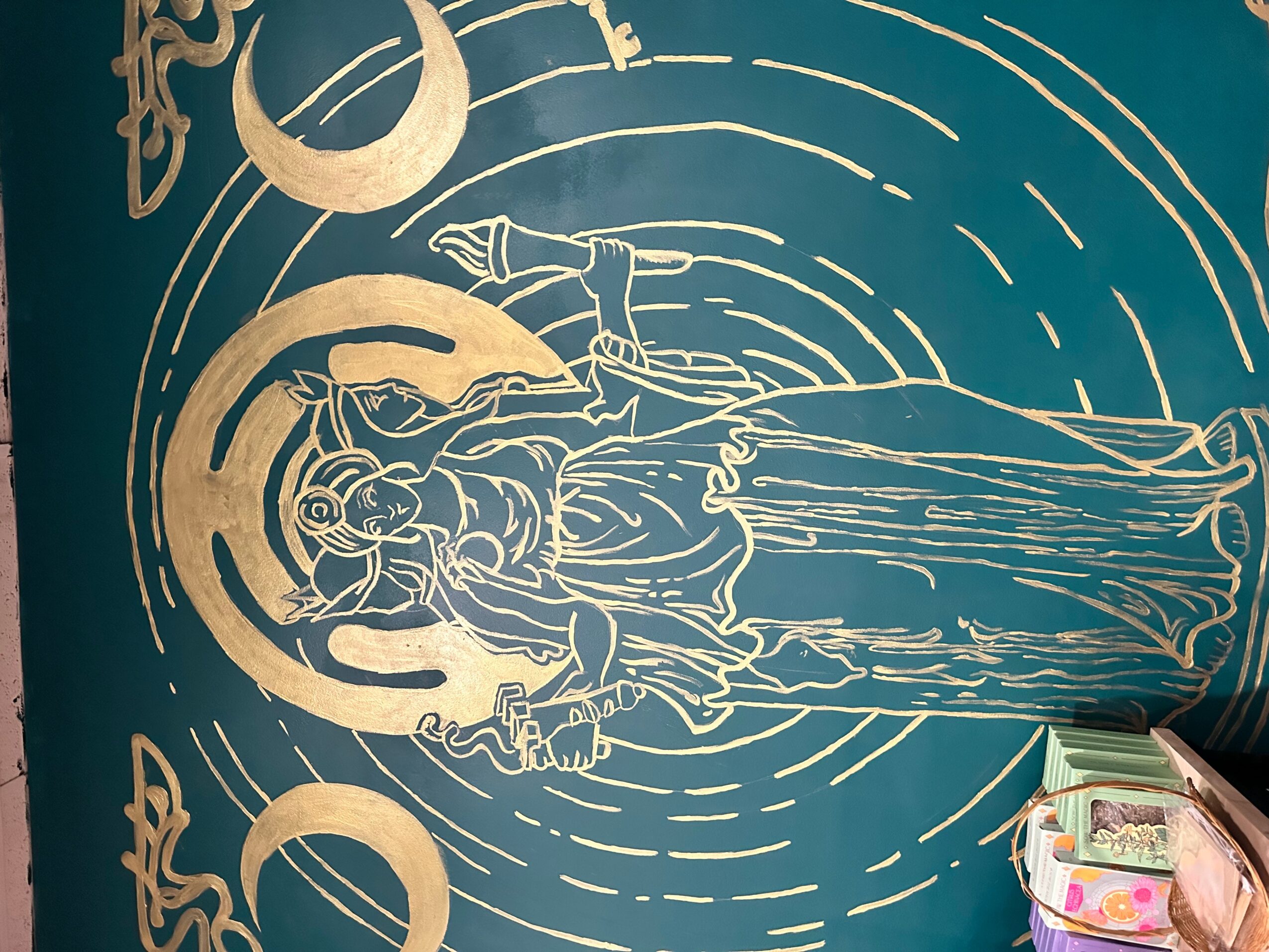 Gold line drawing of a religious figure with a halo, holding a staff, on a blue background, with celestial symbols.