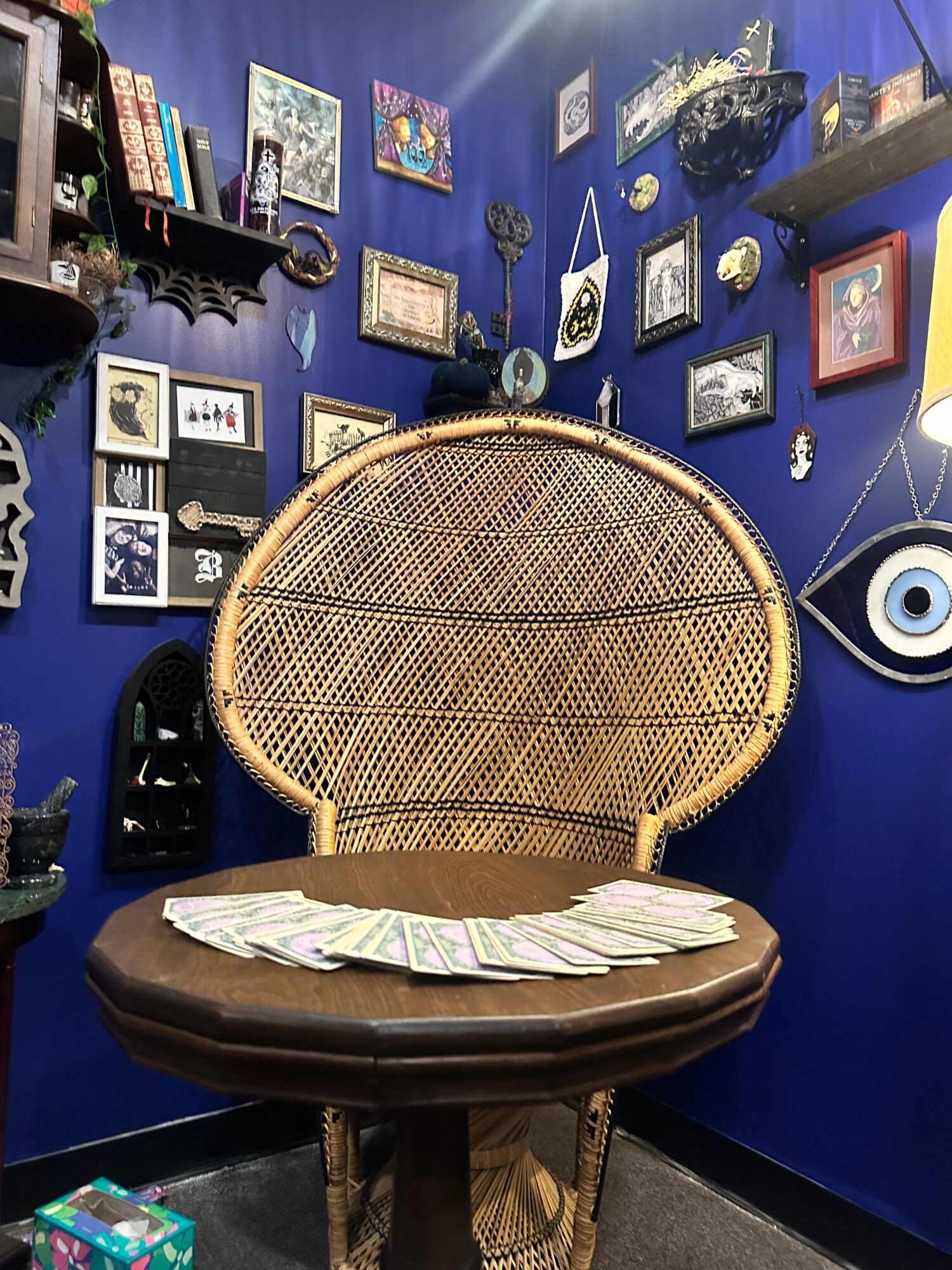 Wicker chair with a round cushion in a room with blue walls decorated with framed pictures and objects.