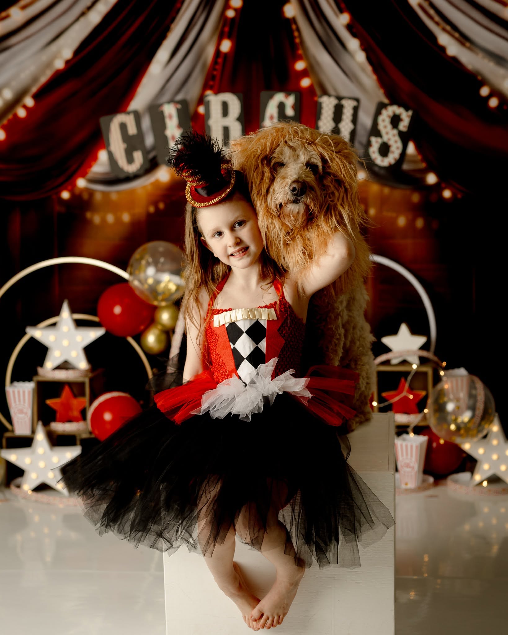 Girl in a black and red costume with a tutu, holding a large dog, in front of circus-themed decorations and a sign that says 'CIRCUS'.