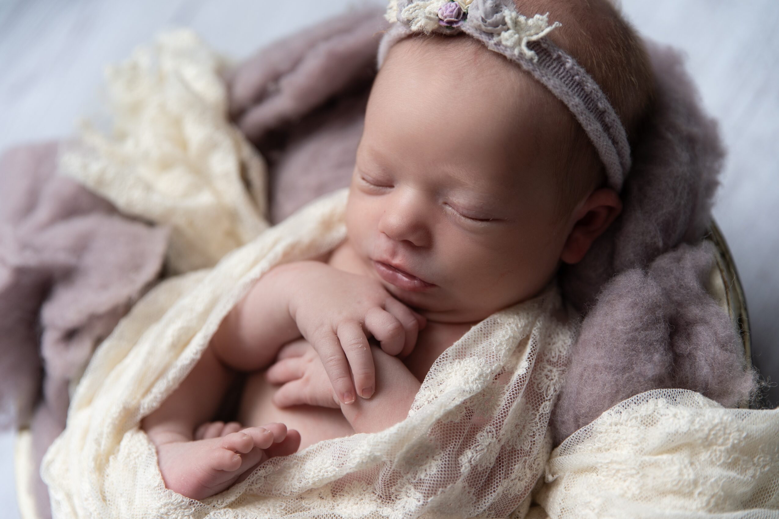 Sleeping baby with a headband, wrapped in soft blankets, resting peacefully.