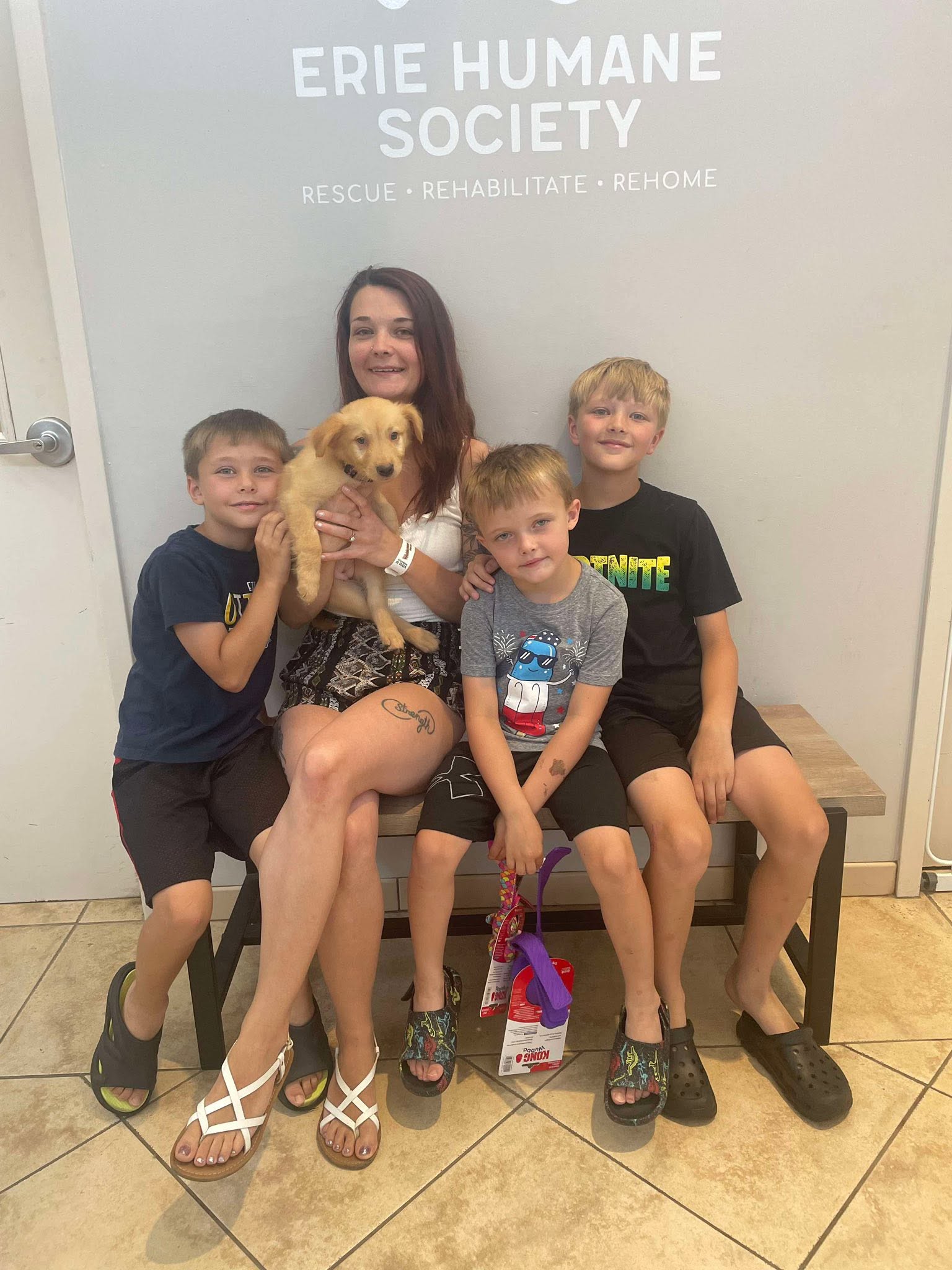 Woman with four children and a puppy sitting on a bench in front of a wall with Erie Humane Society sign.