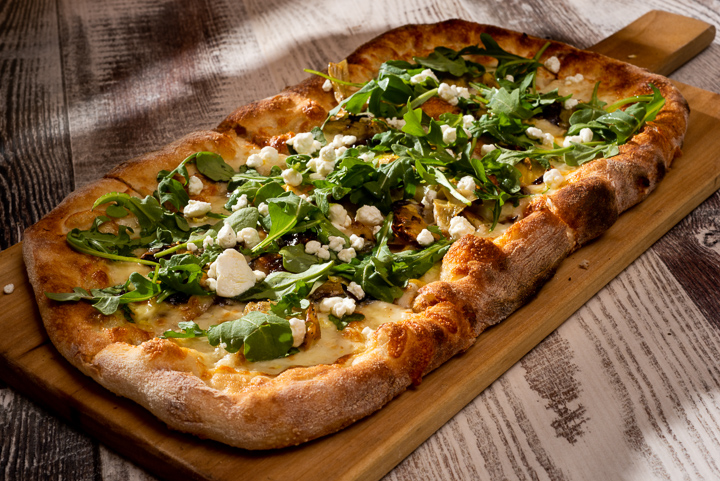 Rectangular pizza topped with arugula, cheese, and nuts on a wooden board, on a rustic table.