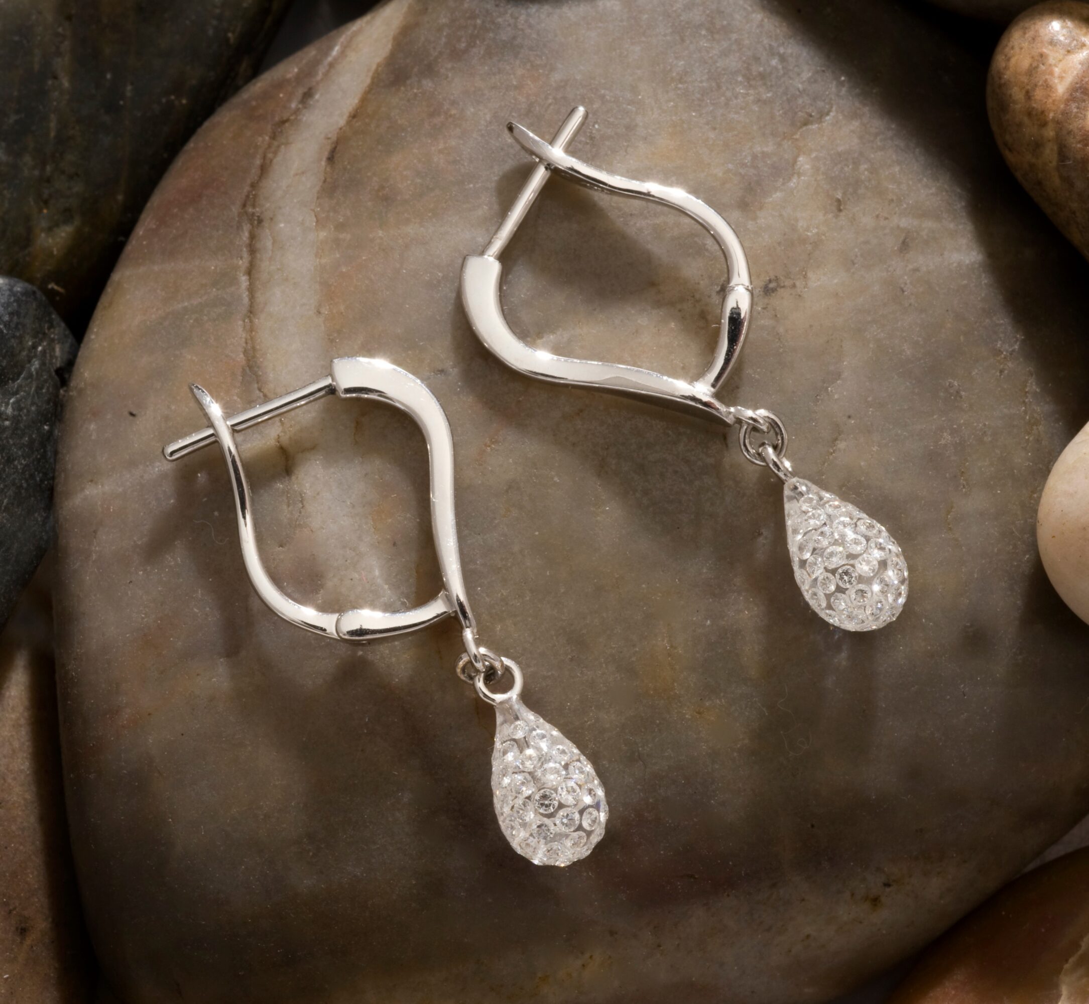 Silver earrings with teardrop-shaped, textured pendants resting on a smooth, round stone surface.