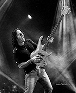 Person playing an electric bass guitar on stage with lighting effects, in black and white.