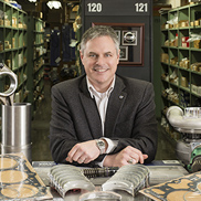 Man sitting at a table in a store, smiling, with shelves of products behind him.