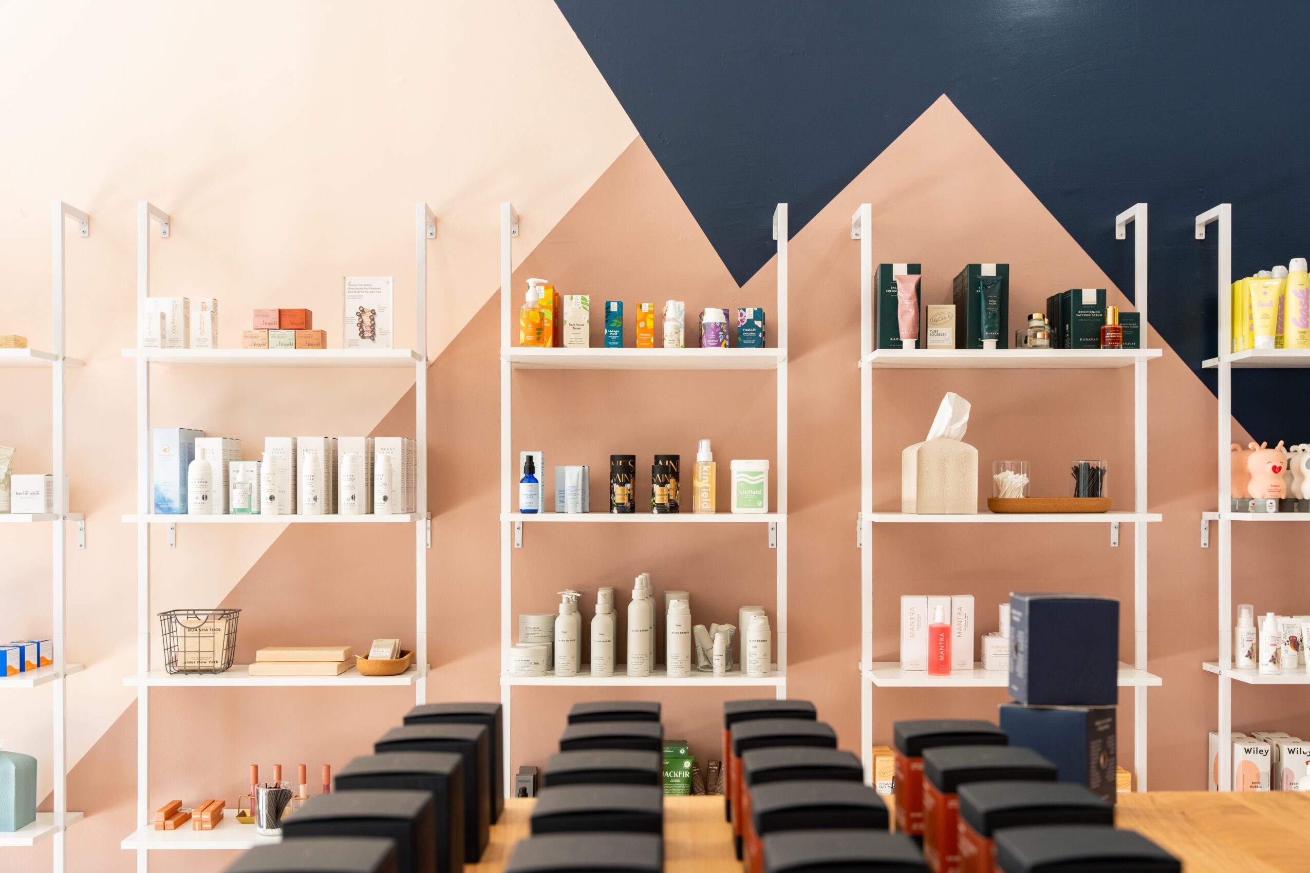 Shelves filled with various products in a store, with black chairs in front, and a geometric wall design in the background.