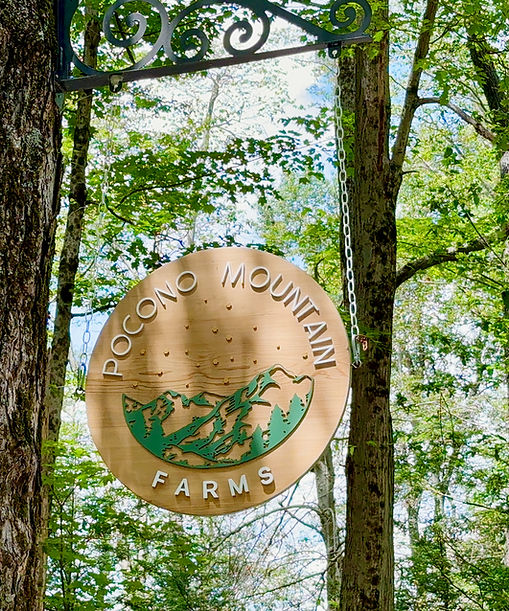 Round sign hanging between trees with green and brown design, reading 'Pocono Mountain Farms'.