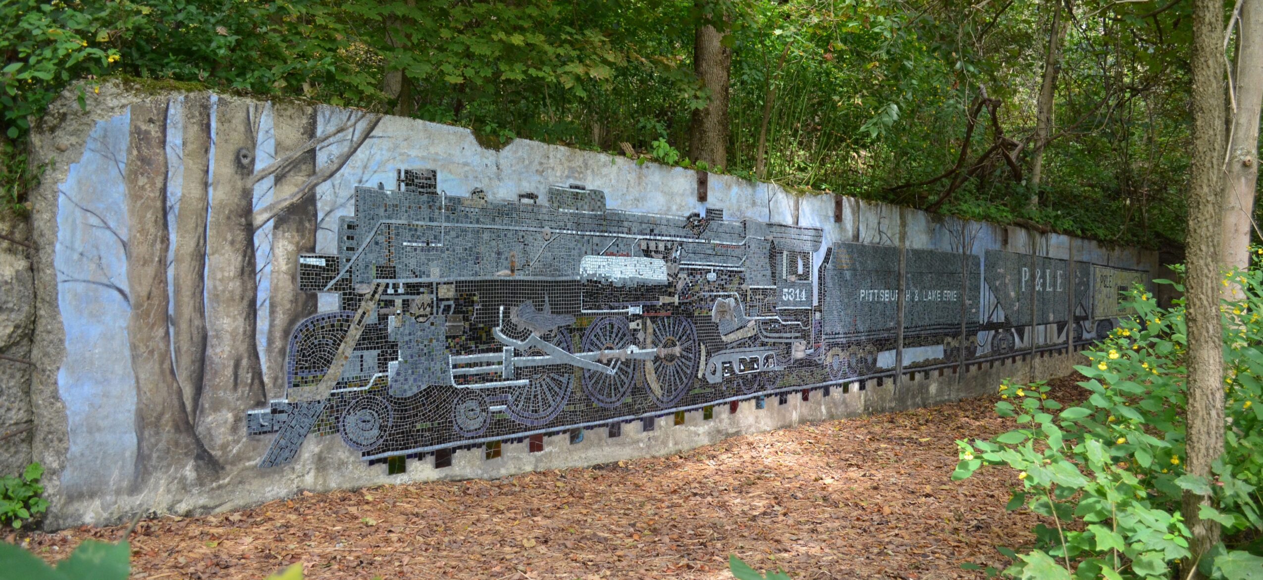 Mural of a vintage steam locomotive painted on a rock wall in a forest setting.