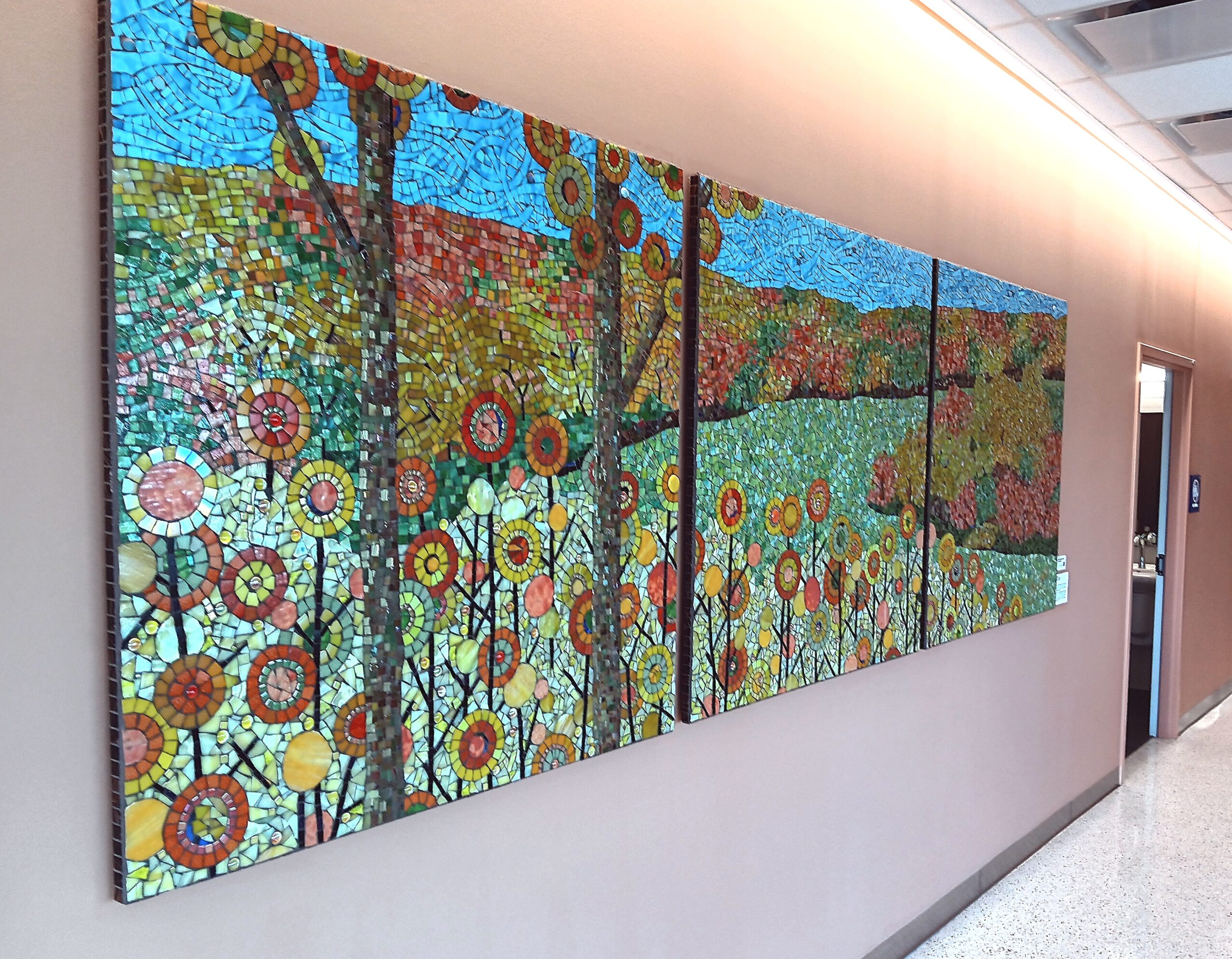Colorful mosaic artwork depicting a vibrant landscape with trees and flowers on a wall, divided into five panels.