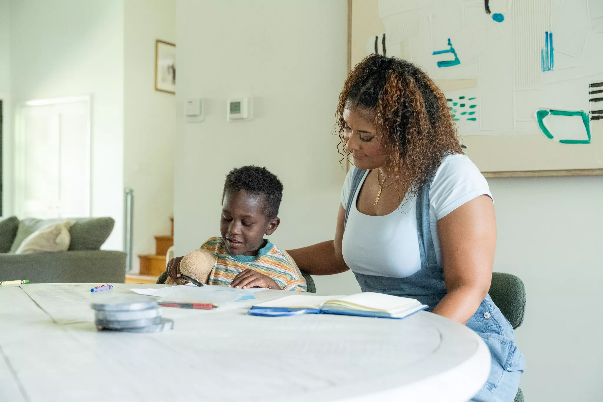 Woman and child sitting at a table reading a book together in a bright room.