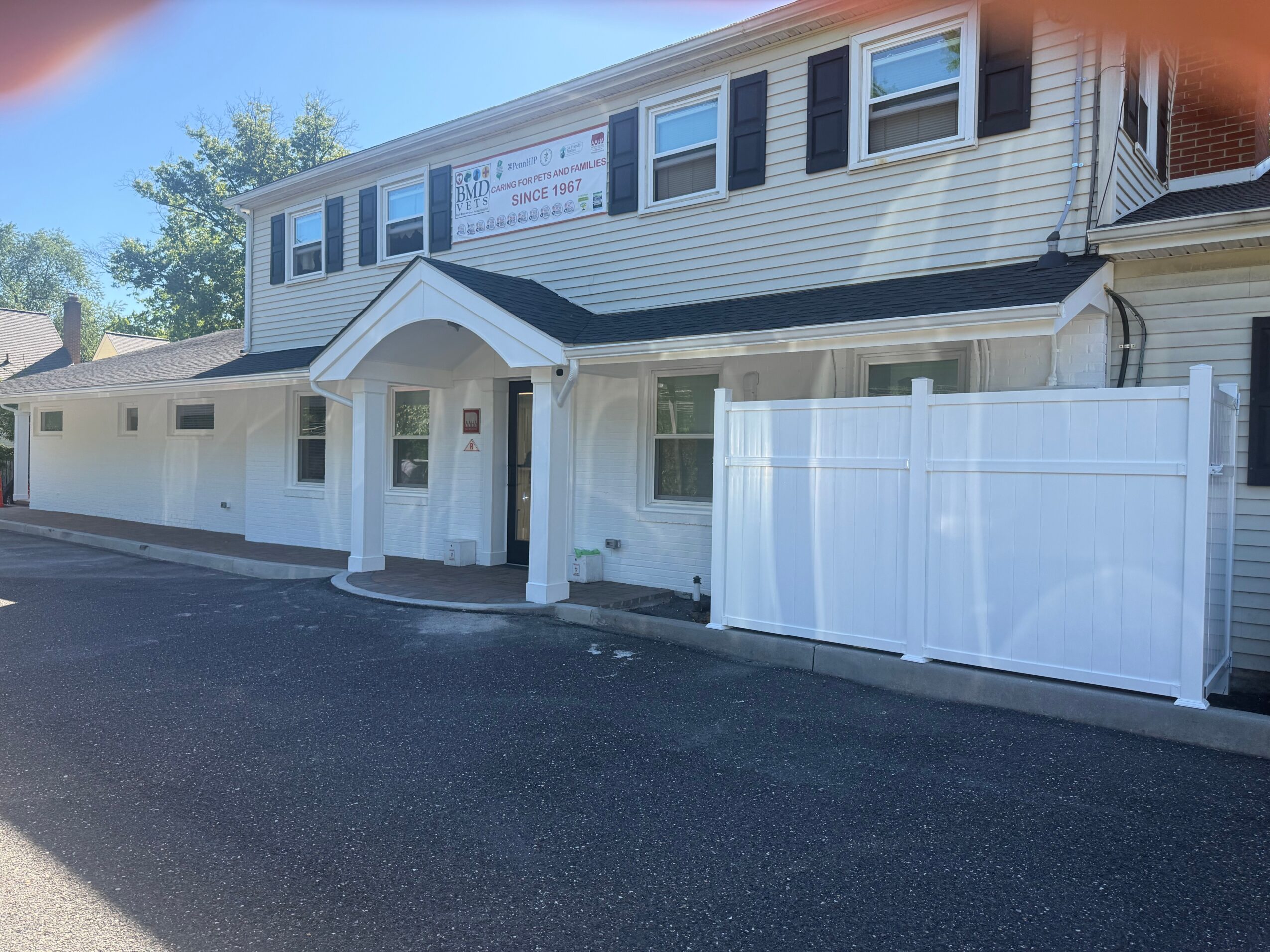 Two-story building with white siding, black shutters, and a white fence, under a clear blue sky.