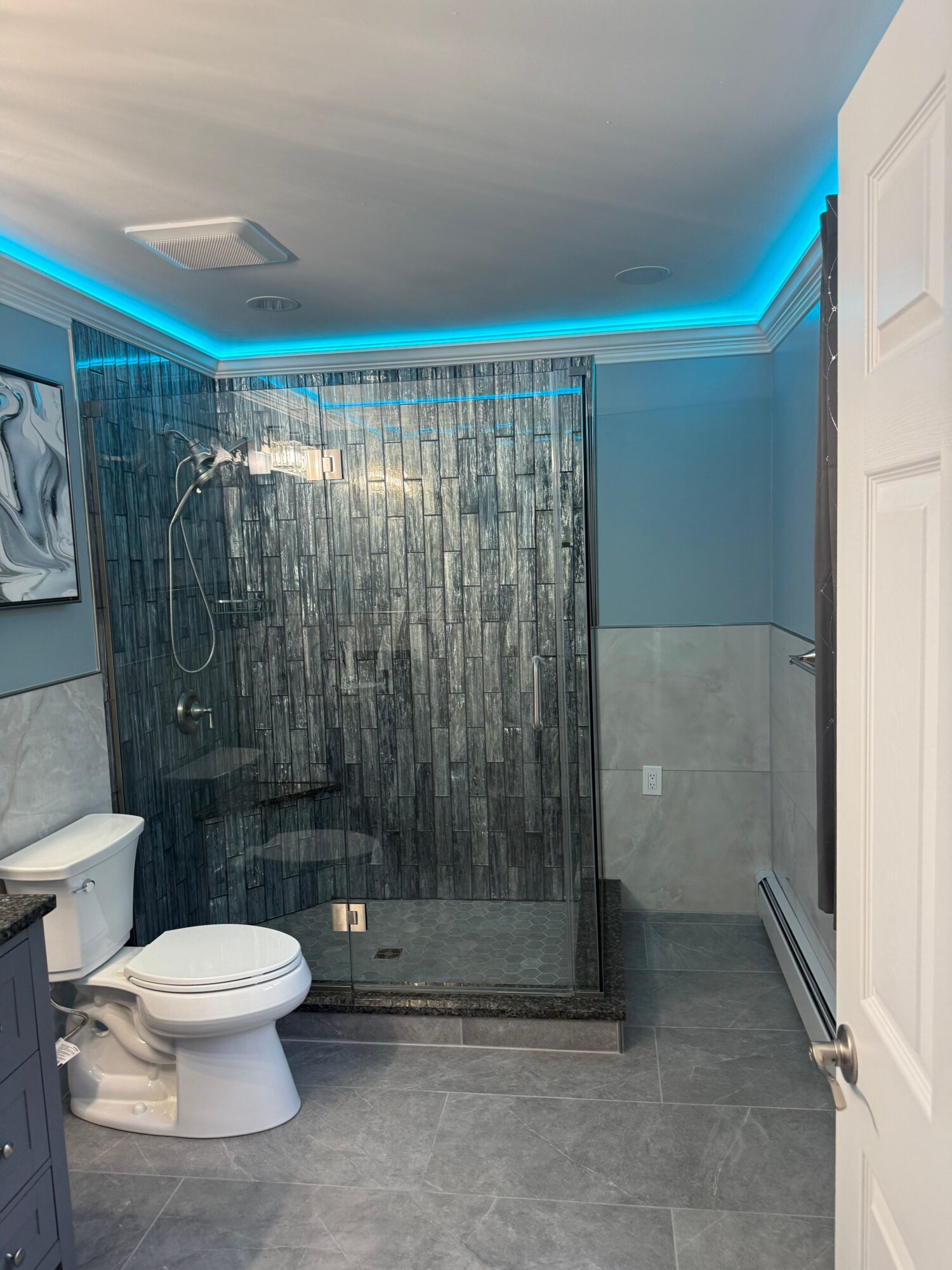 Bathroom with gray tiled floor, toilet, and a textured gray wall with blue LED lighting, viewed from the doorway.