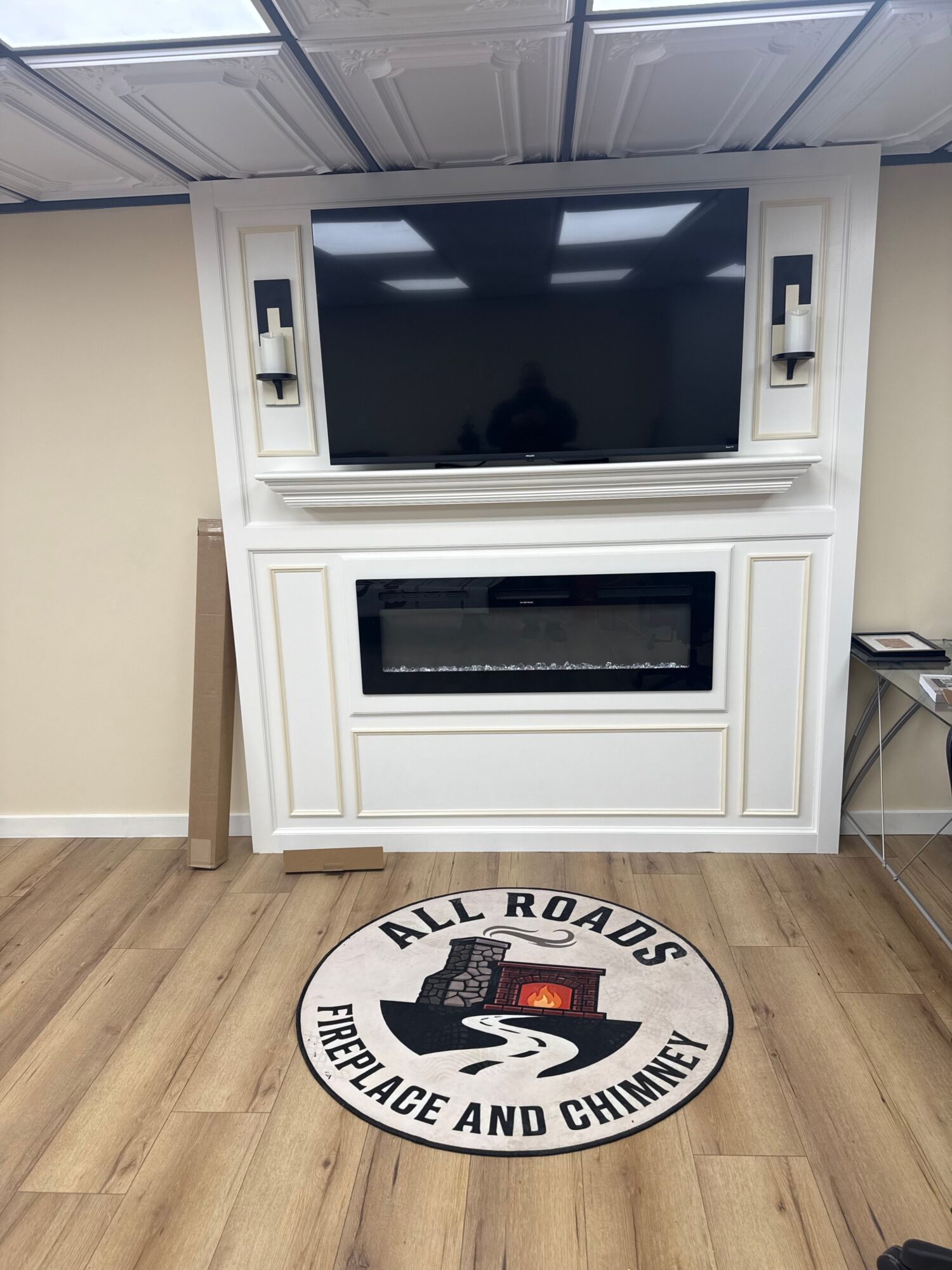 White fireplace with a black insert, positioned on a wooden floor, with a circular decorative piece nearby.