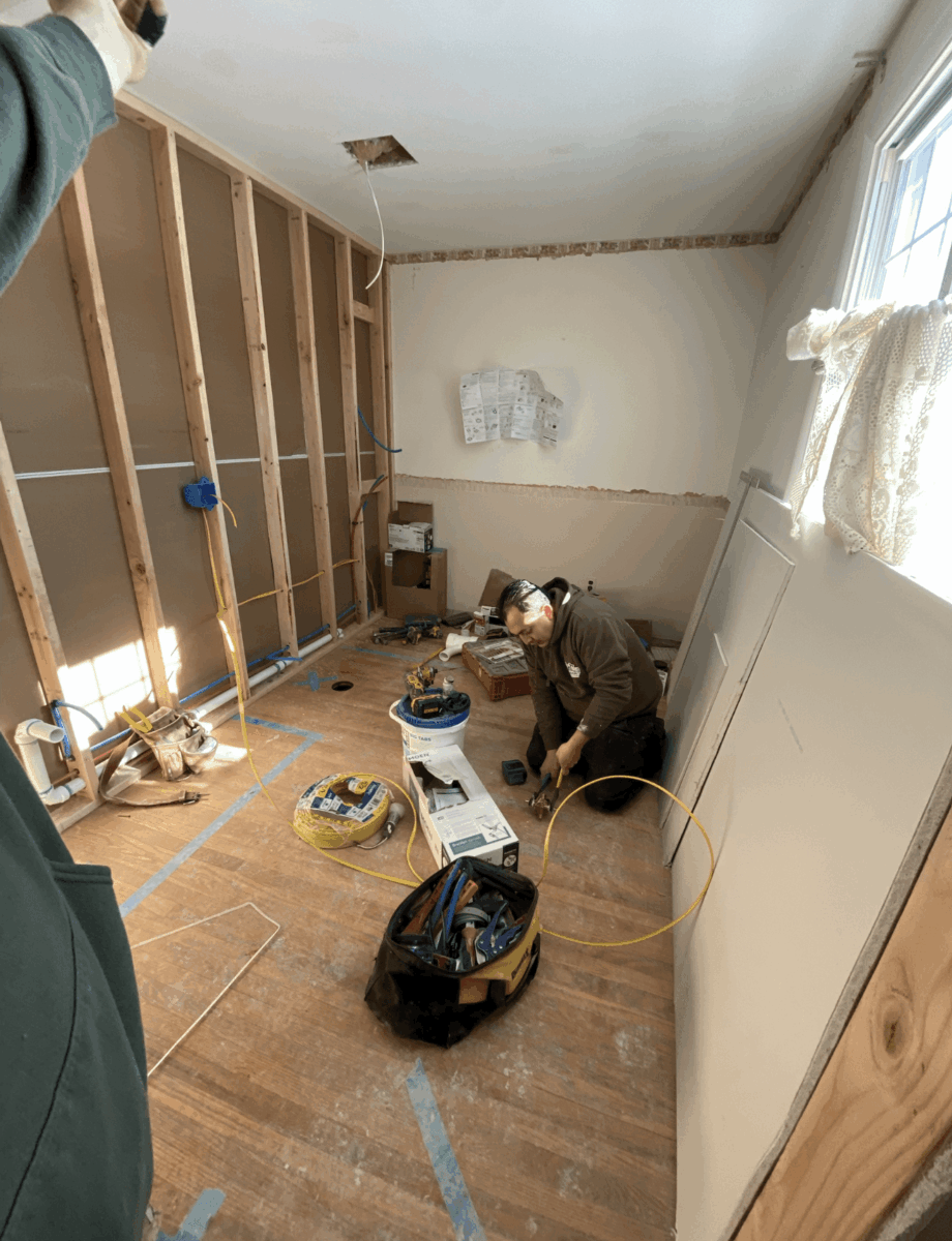 Room under construction with wooden framing, tools, and a person working, window with curtains, and a whiteboard on the wall.