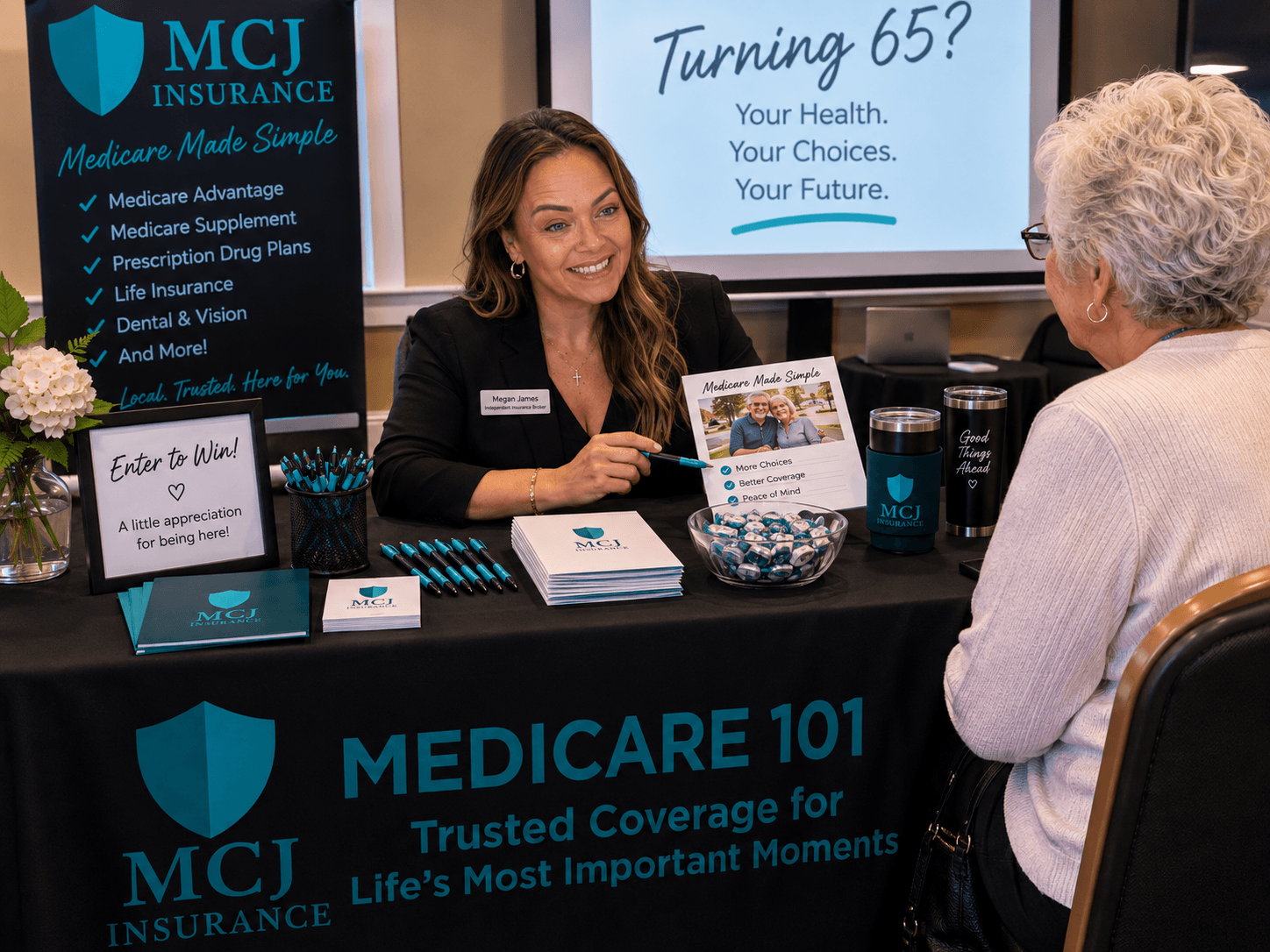 A woman at a booth talking to an elderly woman, with a sign celebrating turning 65 in the background.