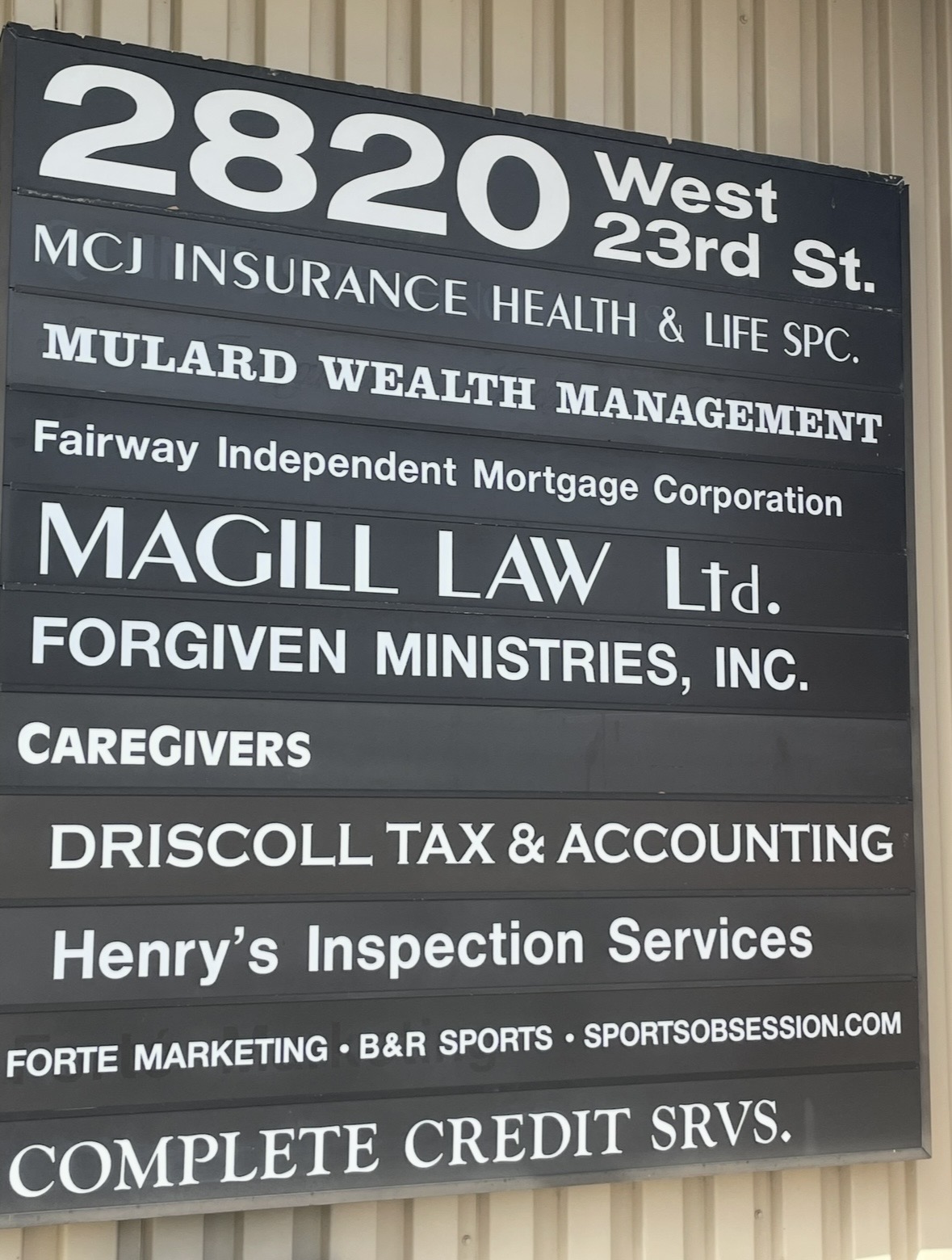 Black and white business sign with multiple company names and services listed, including insurance, law, and accounting, at 2820 West 23rd Street.