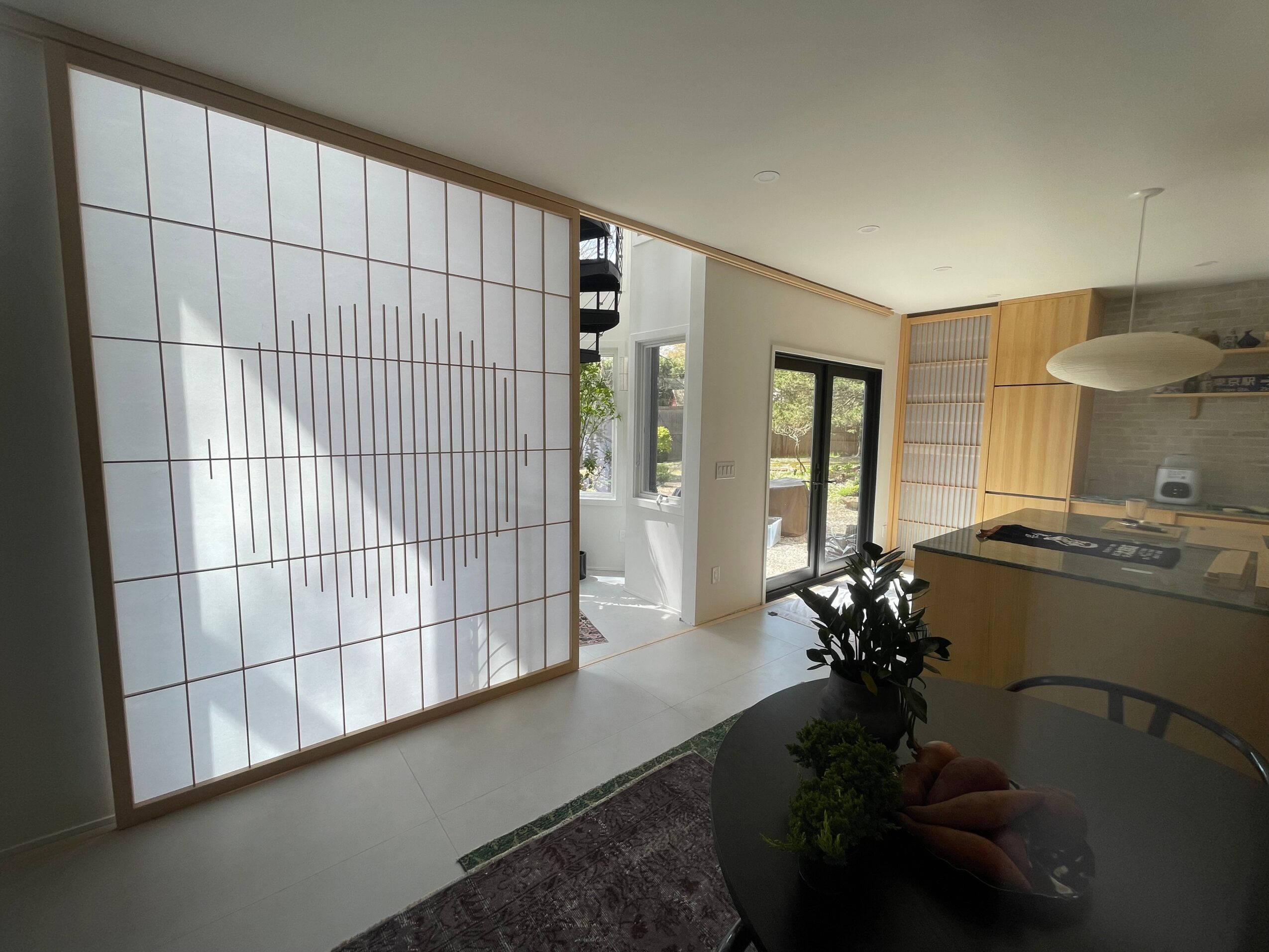 Living room with large sliding glass doors, wooden accents, and a dining table with a plant centerpiece.