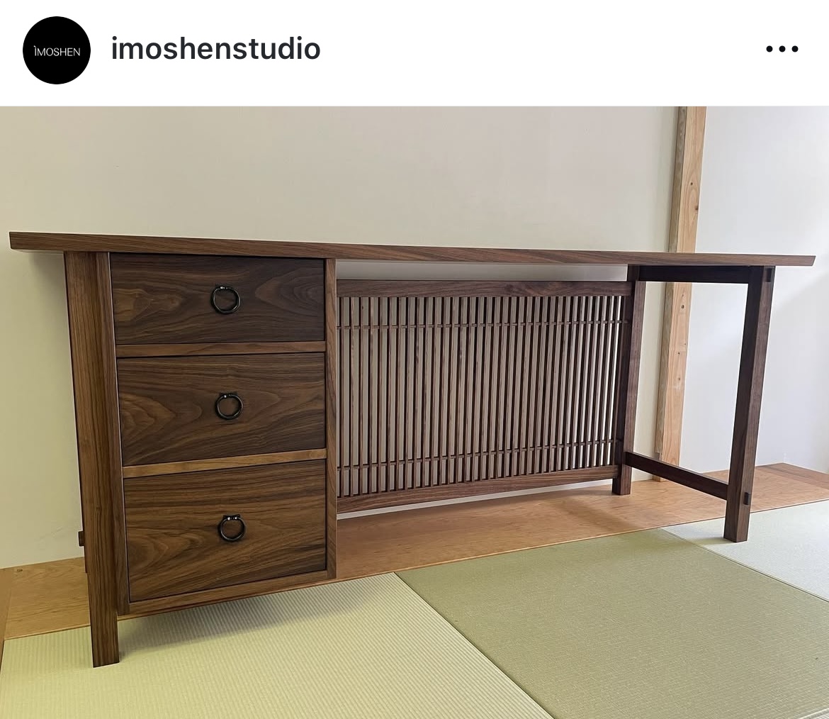 Wooden desk with three drawers on the left and a slatted panel on the right, against a light-colored wall.